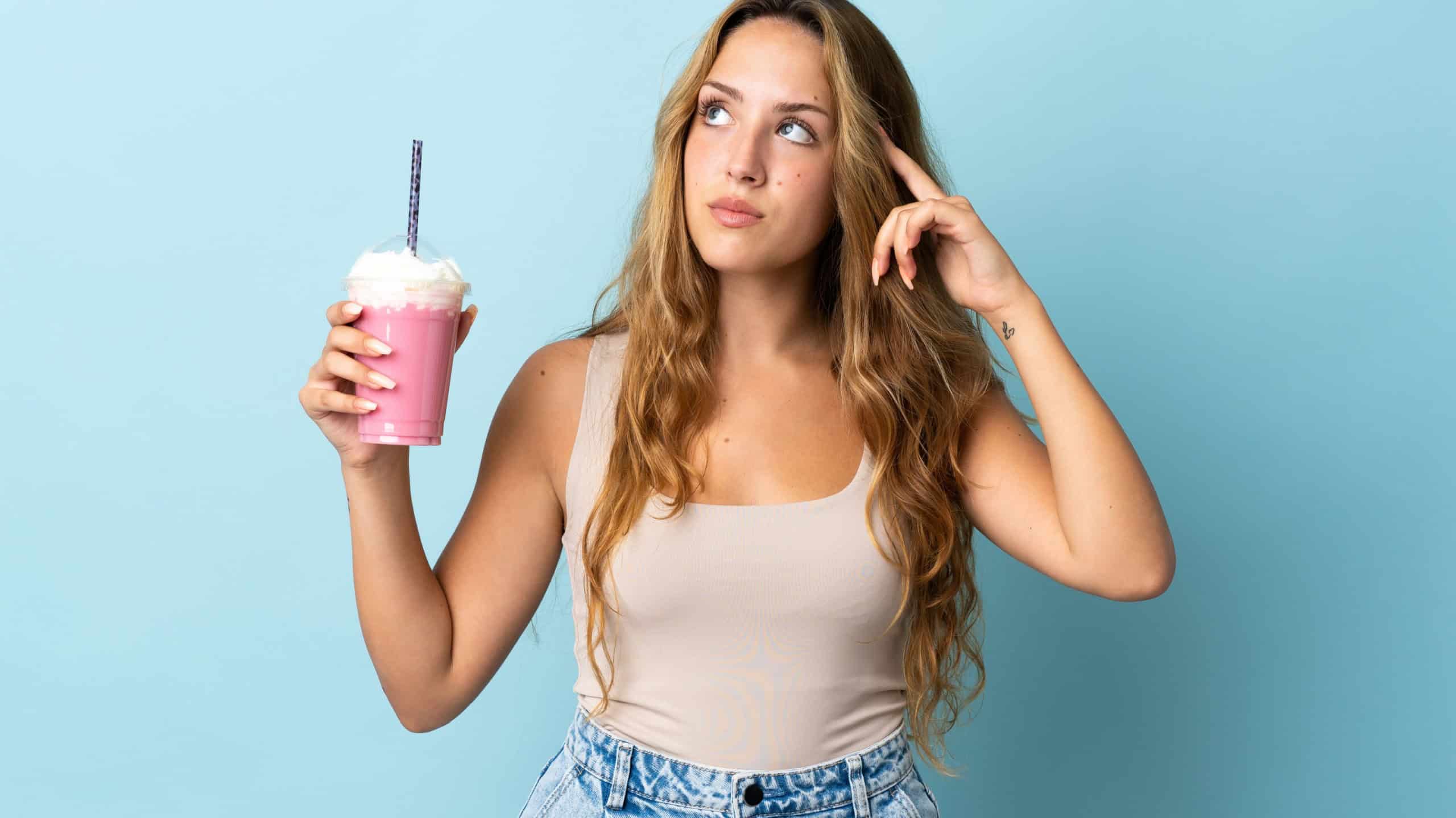 Young woman with strawberry milkshake isolated on blue background having doubts and thinking