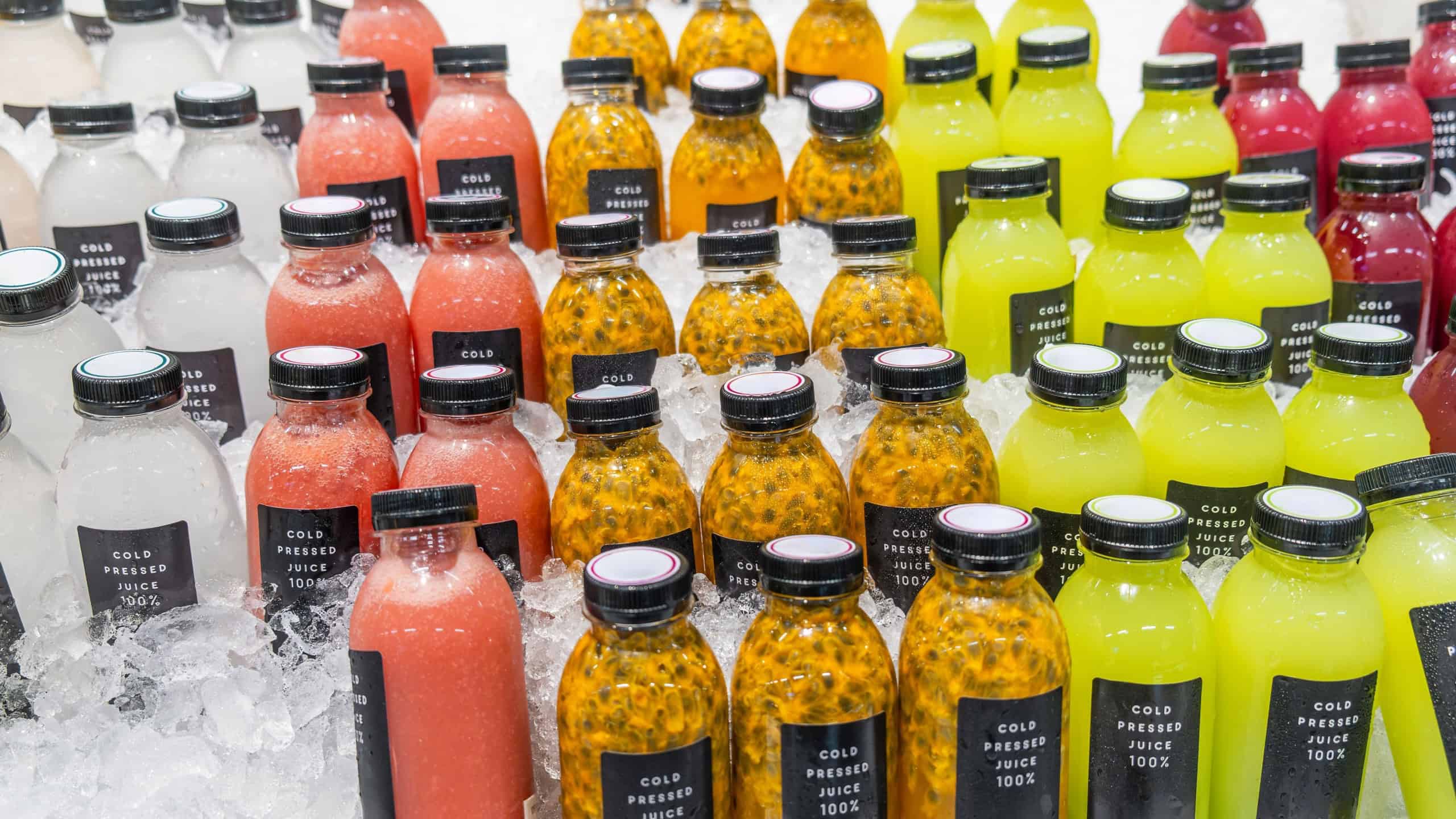 Colorful cold pressed juices in bottles displayed on crushed ice in supermarket shelf. Healthy tropical fruit juice, chilled beverages ready for purchase in grocery store in Thailand. Drink retail