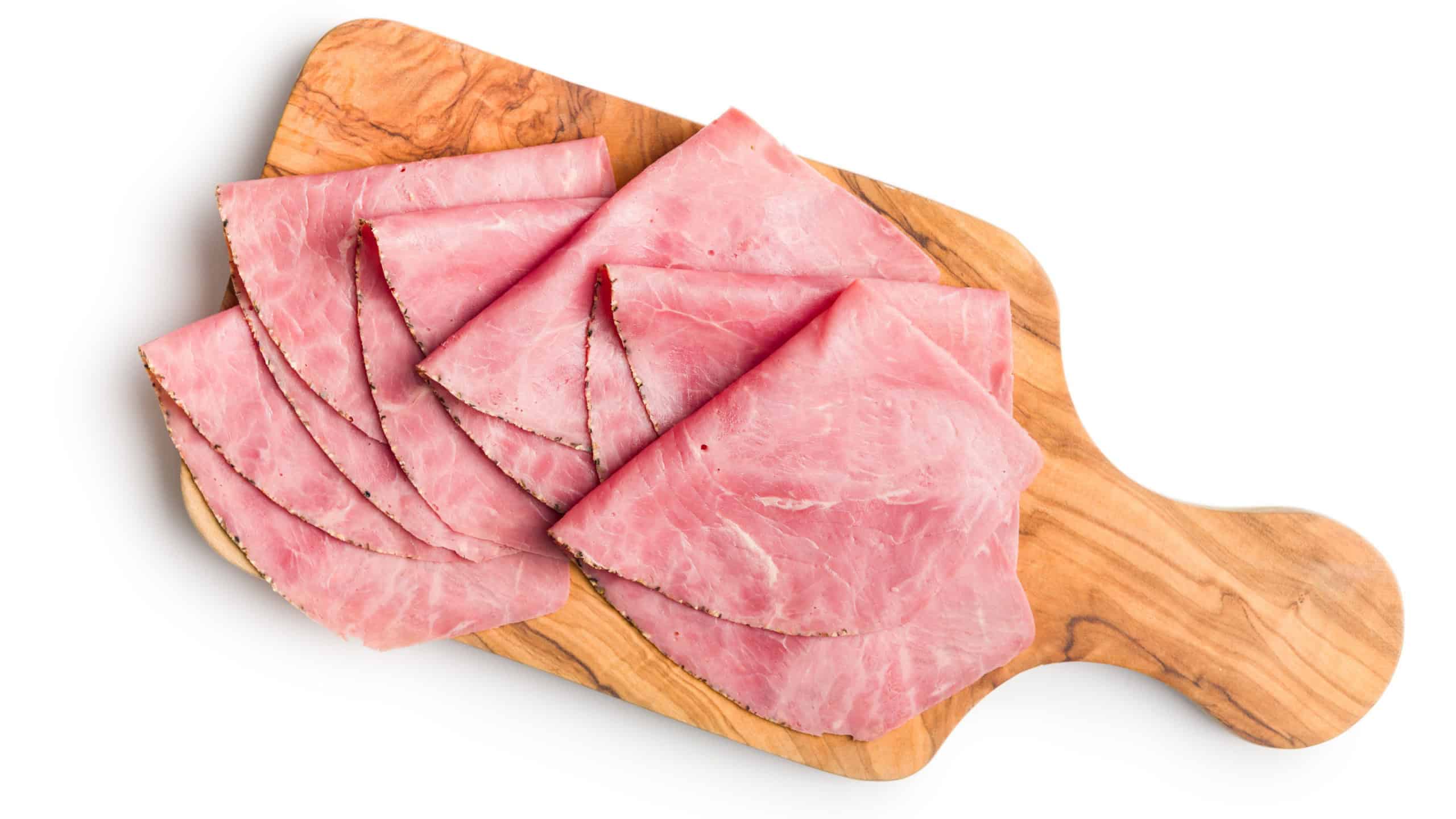 Sliced beef pastrami on cutting board isolated on a white background.