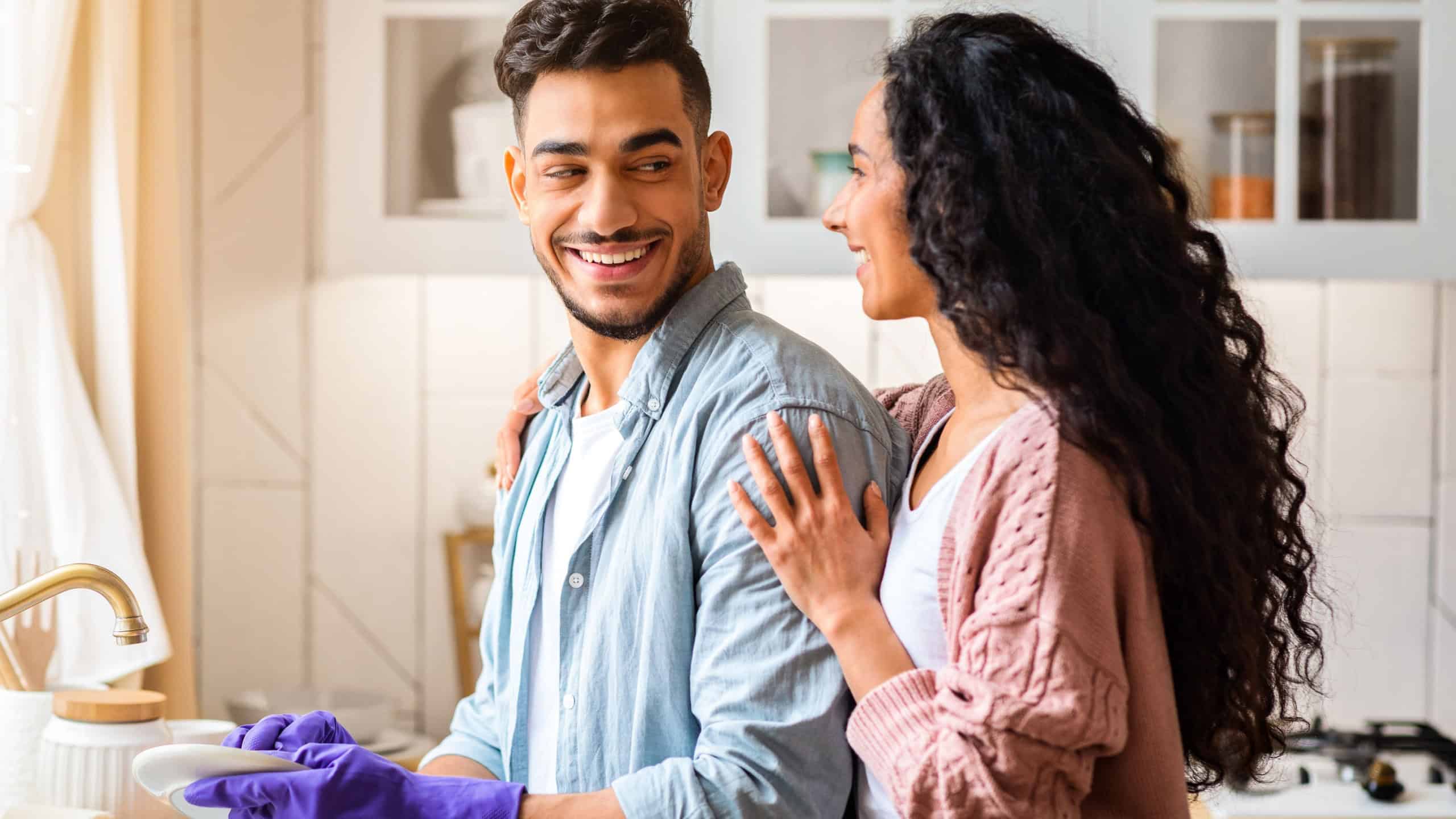 Loving Arab Wife Embracing Her Husband While He Washing Dishes In Kitchen