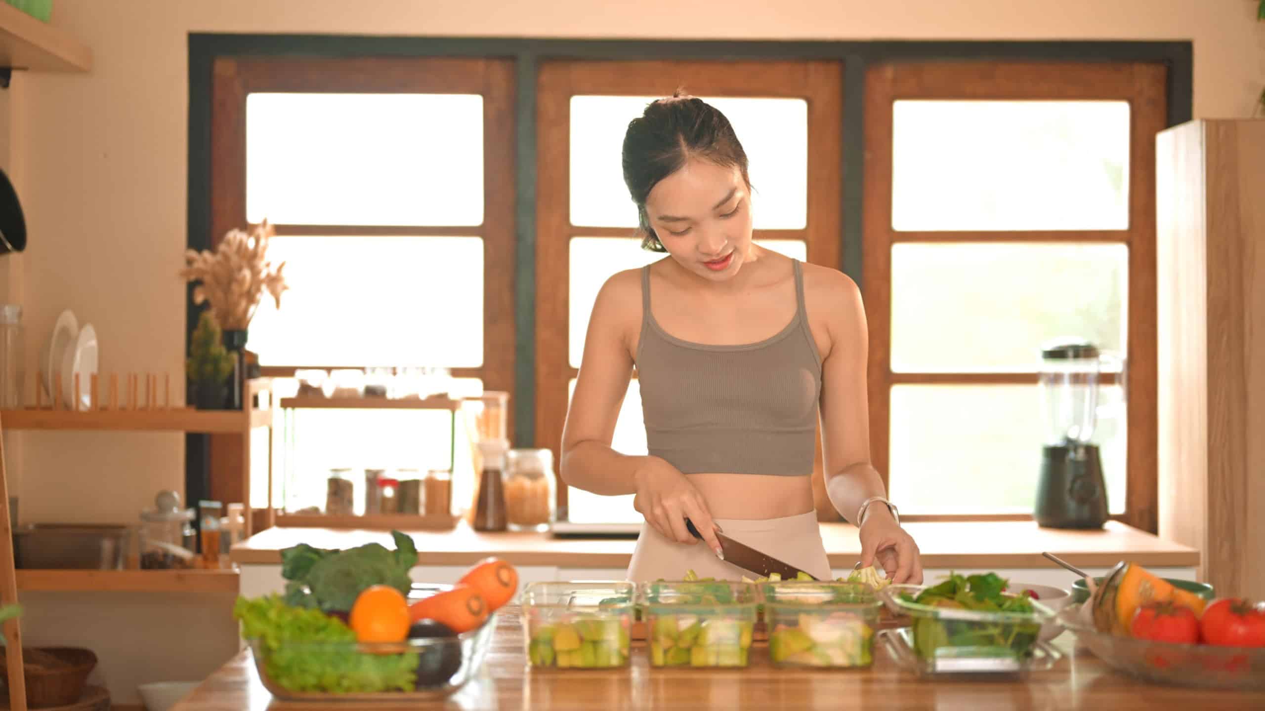 Woman chopping broccoli and dividing food into meals weekend meal prep for weight loss..