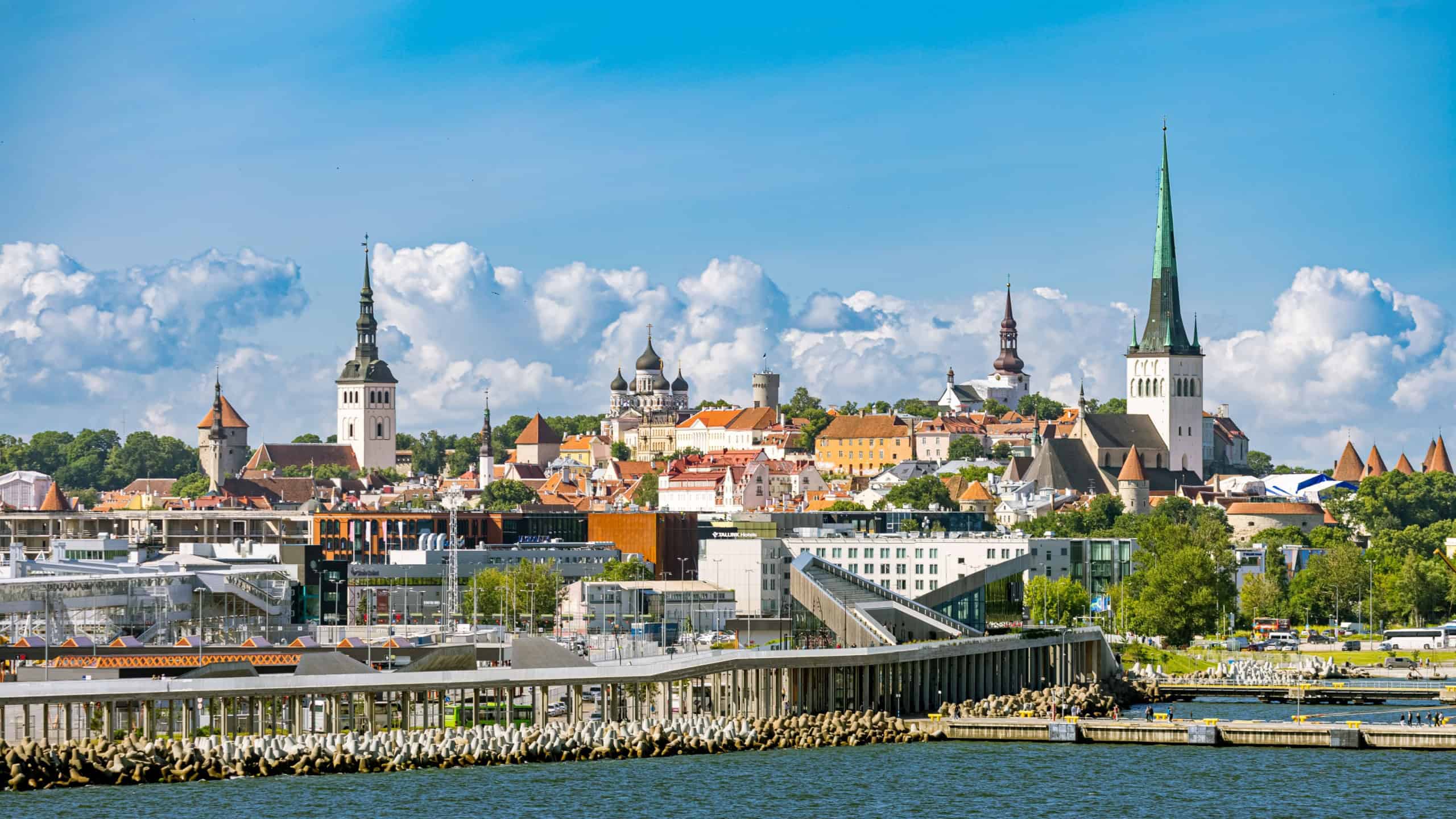  A scenic view of Tallinn's skyline from the sea, showcasing the historic Old Town with its numerous spires and domes on a hill, overlooking modern waterfront building