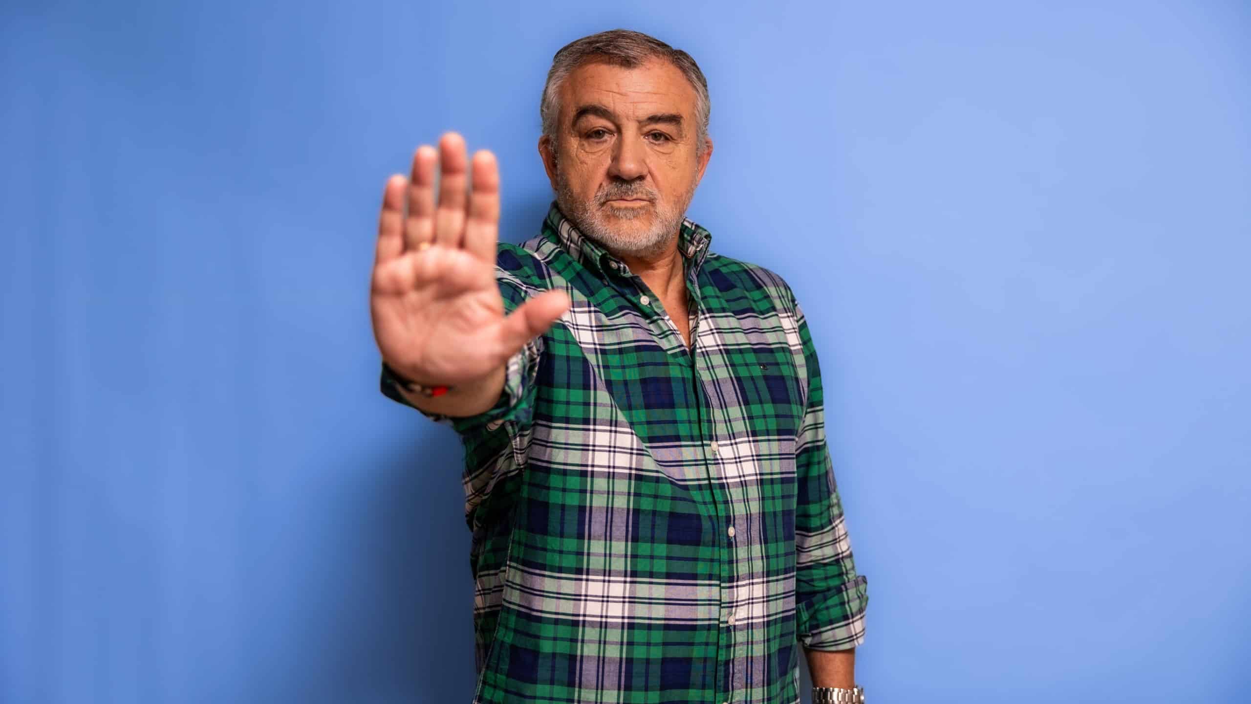 Serious elderly man facing the camera, extending his hand forward in a clear stop gesture, conveying concepts of refusal, warning, and rejection against a blue background