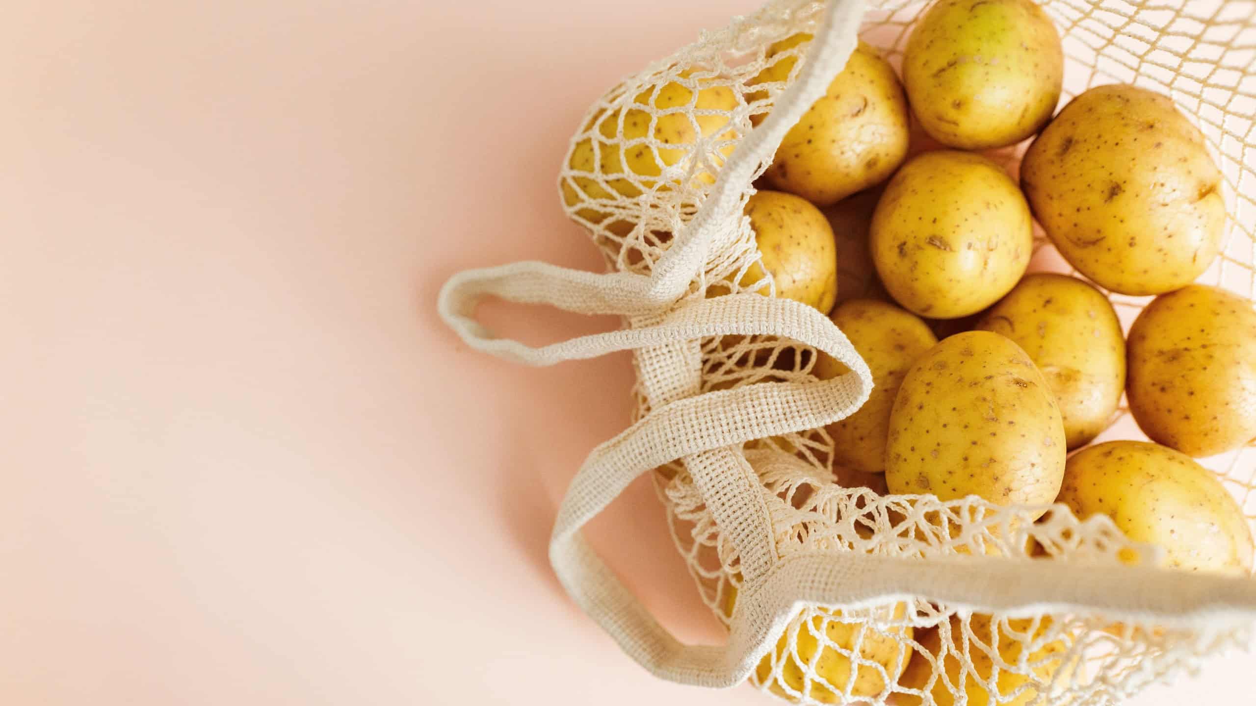 Yellow potatoes inside a reusable white mesh bag showing sustainable grocery shopping habits on a soft pink background