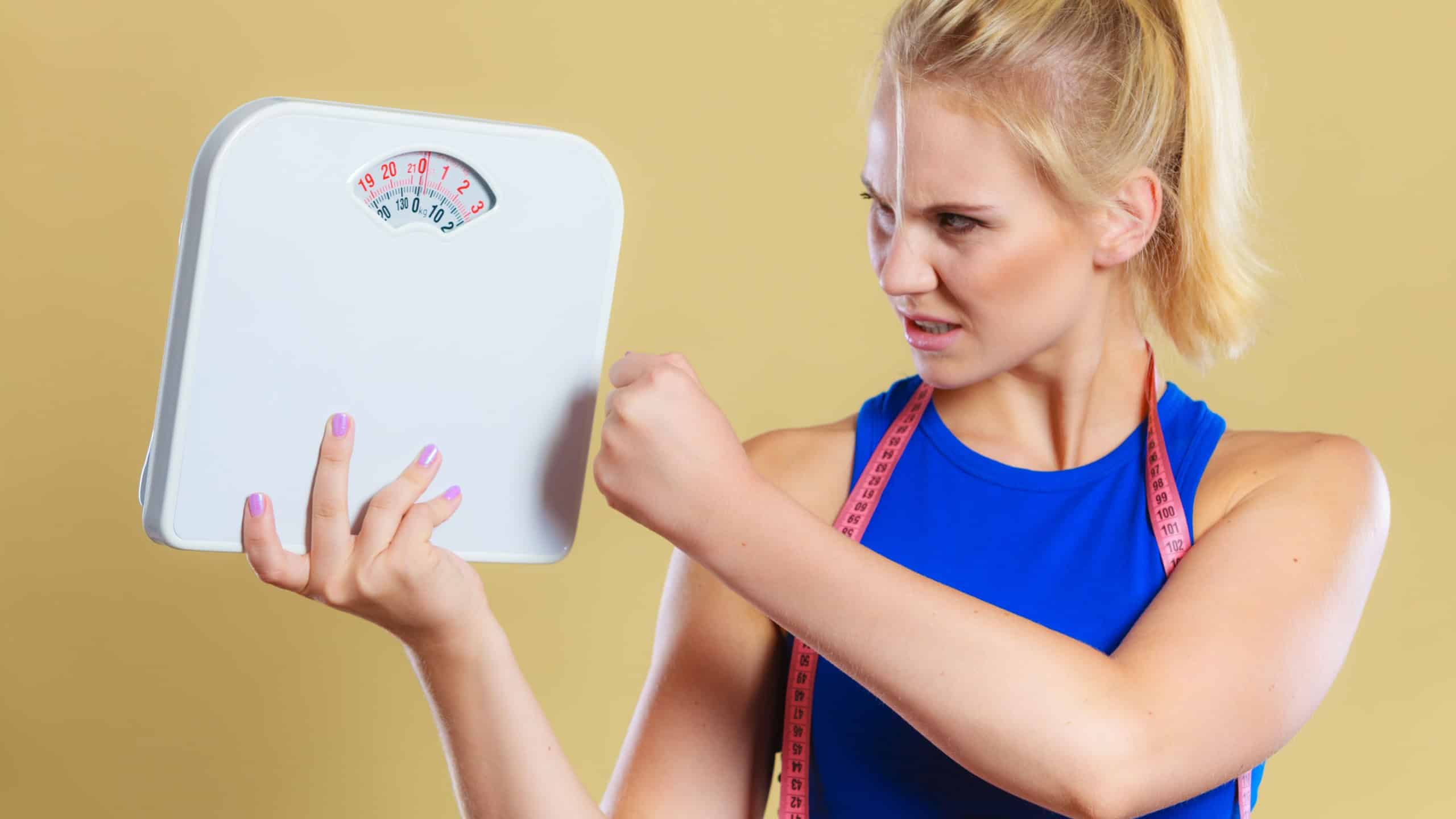 Fit fitness woman with scale. Frustrated angry blonde girl holding weight scales. Time for slimming weightloss, diet and healthy lifestyles concept