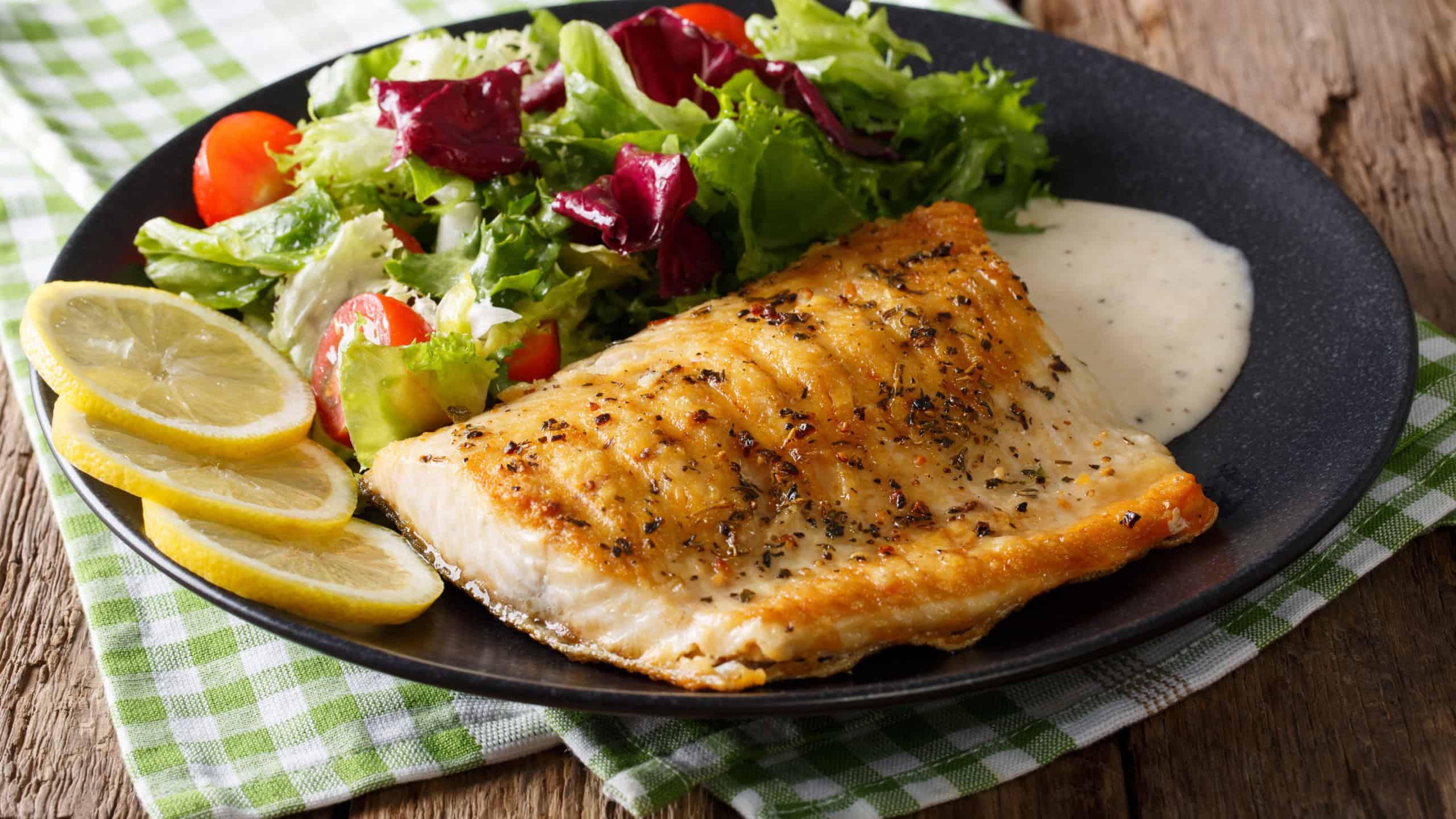 Grilled Arctic char fillet with mixed salad and sauce on a plate close-up