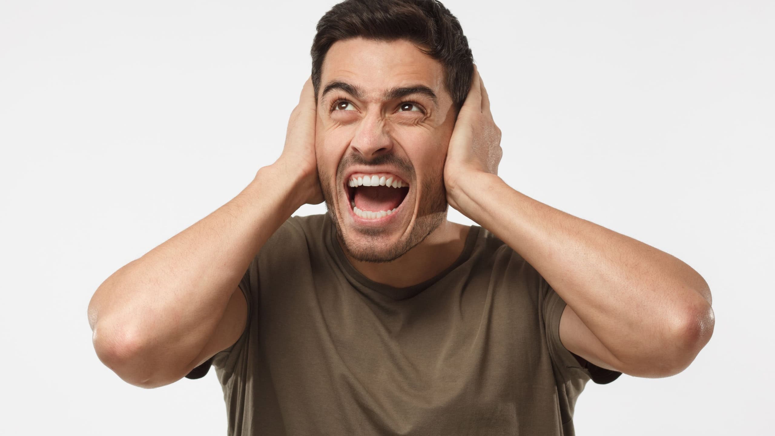 Young handsome man shout at noisy neighbours, stressed by noise, closing ears with both hands, avoid listening fight