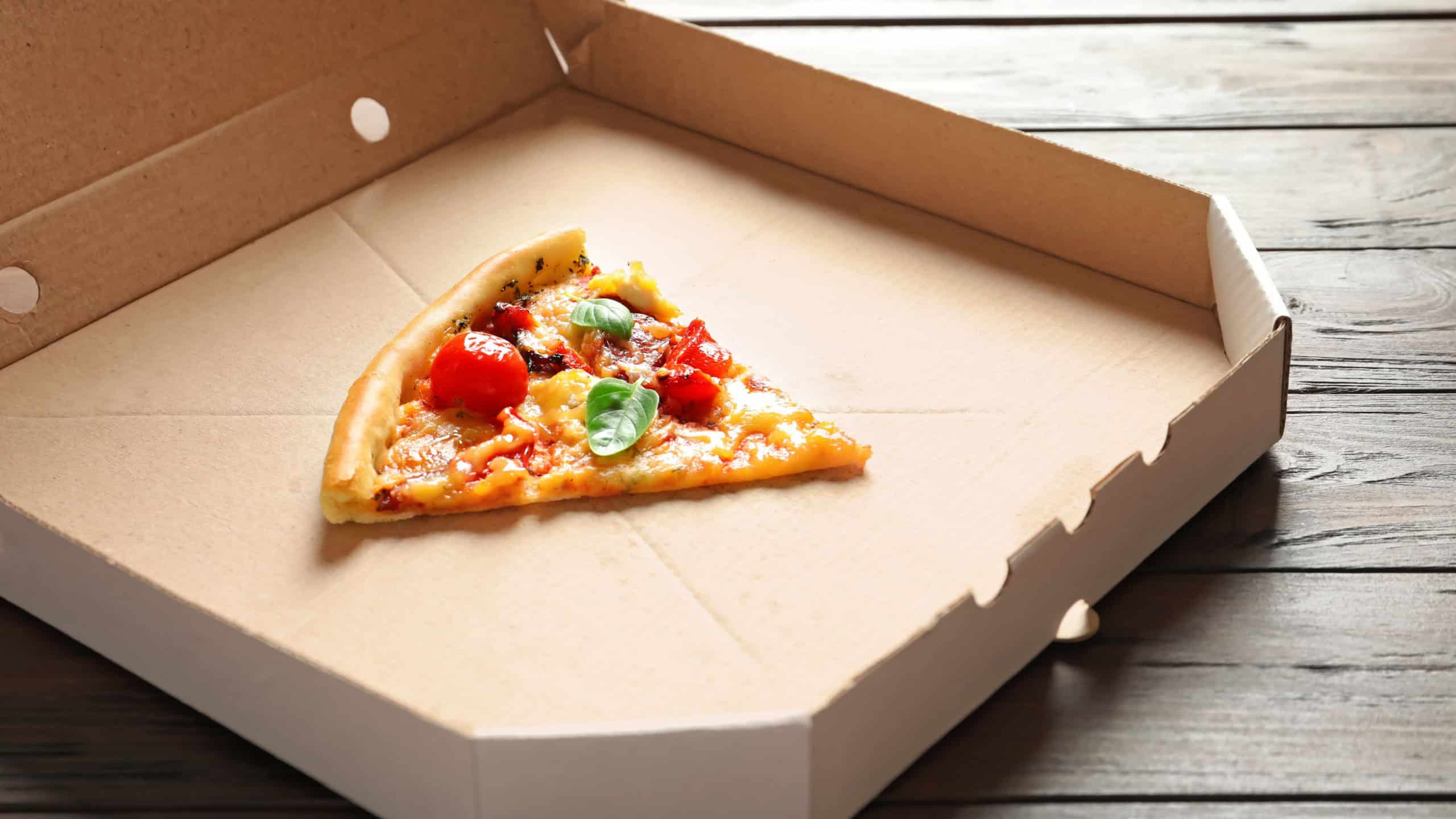 Last slice of tasty pizza in cardboard box on table