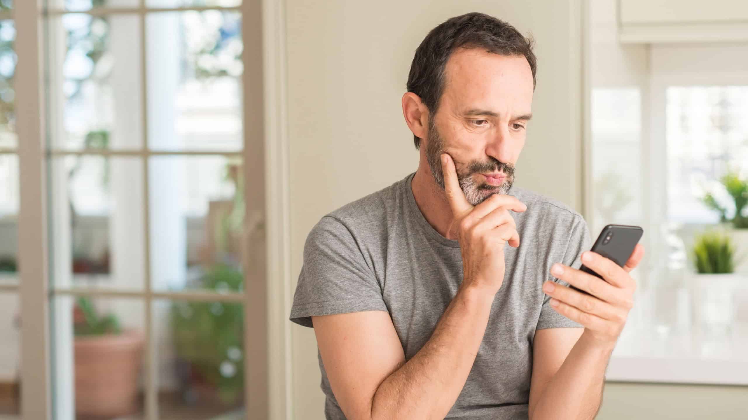 Middle age man using smartphone serious face thinking about question, very confused idea