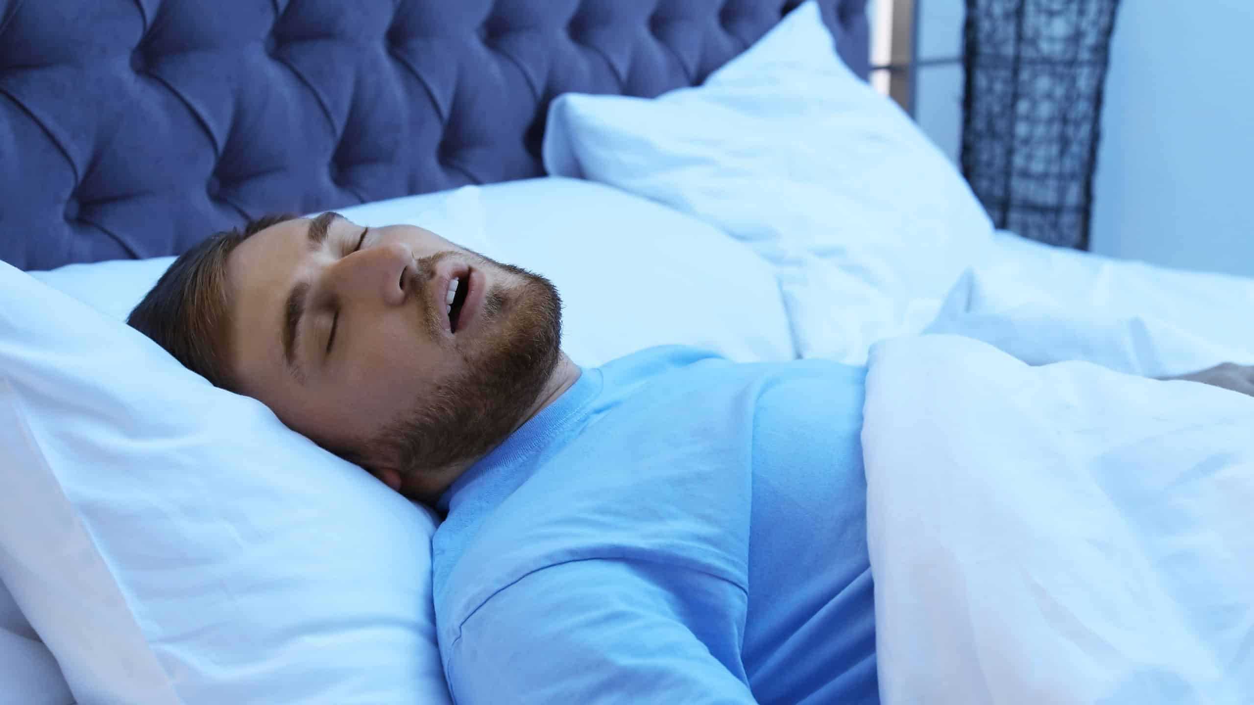 Young man snoring while sleeping in bed at night. Sleep disorder
