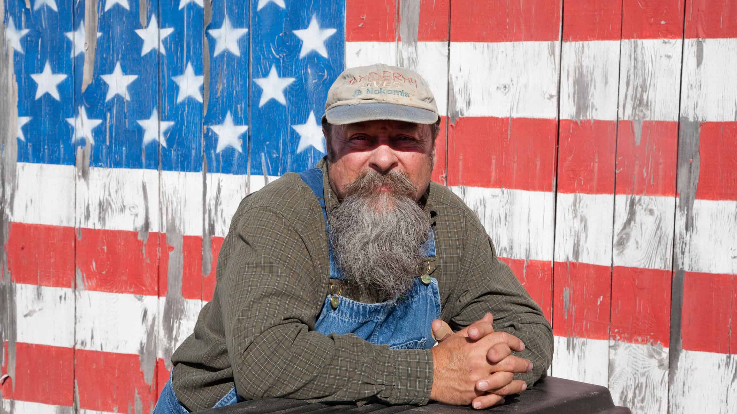 AUGUSTA - JUNE 10: Elderly man poses in front of US flag painted on a barn door on June 10, 2012 near Augusta, Maine