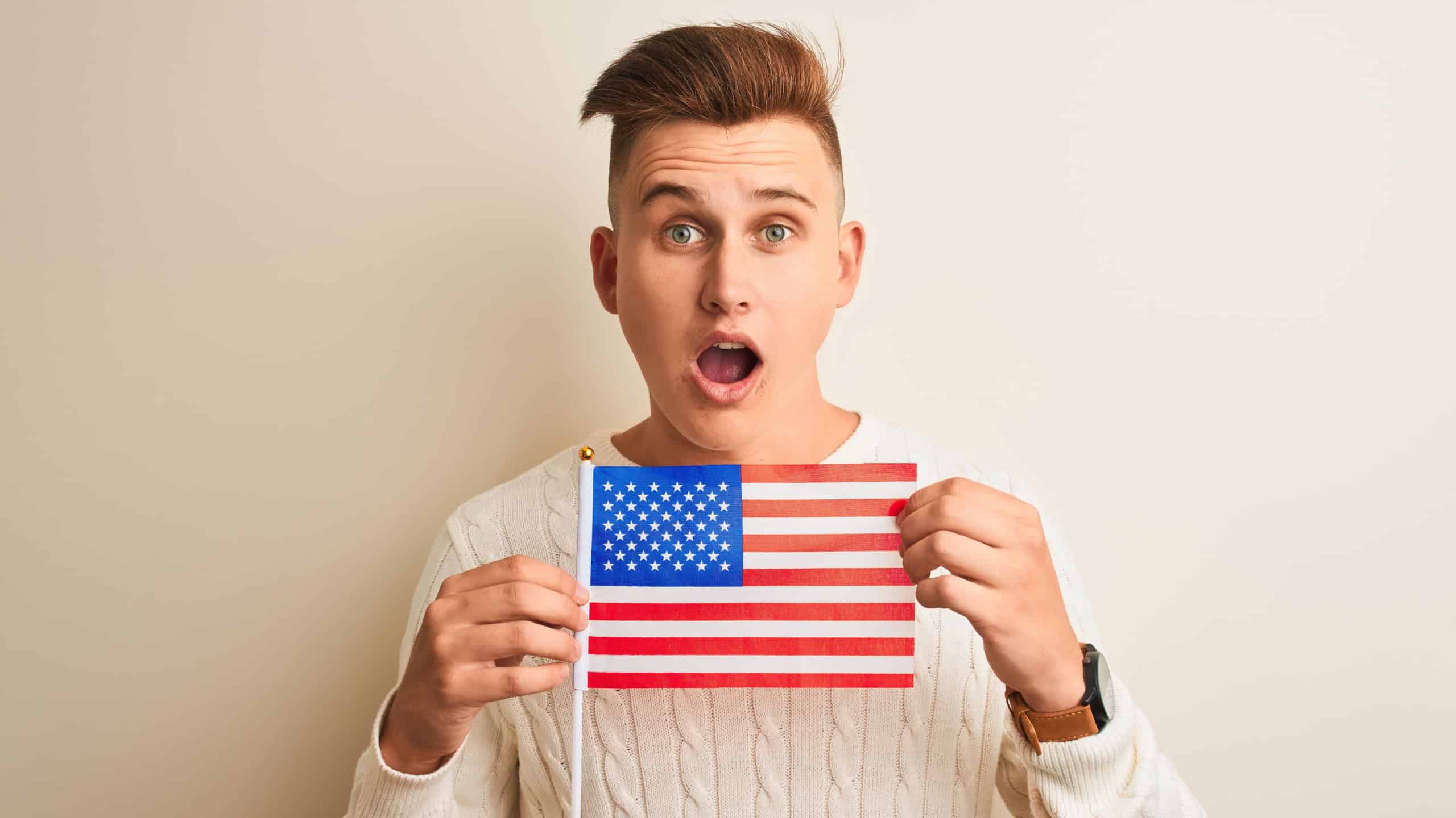 Young handsome man holding USA flag over isolated white background scared in shock with a surprise face, afraid and excited with fear expression