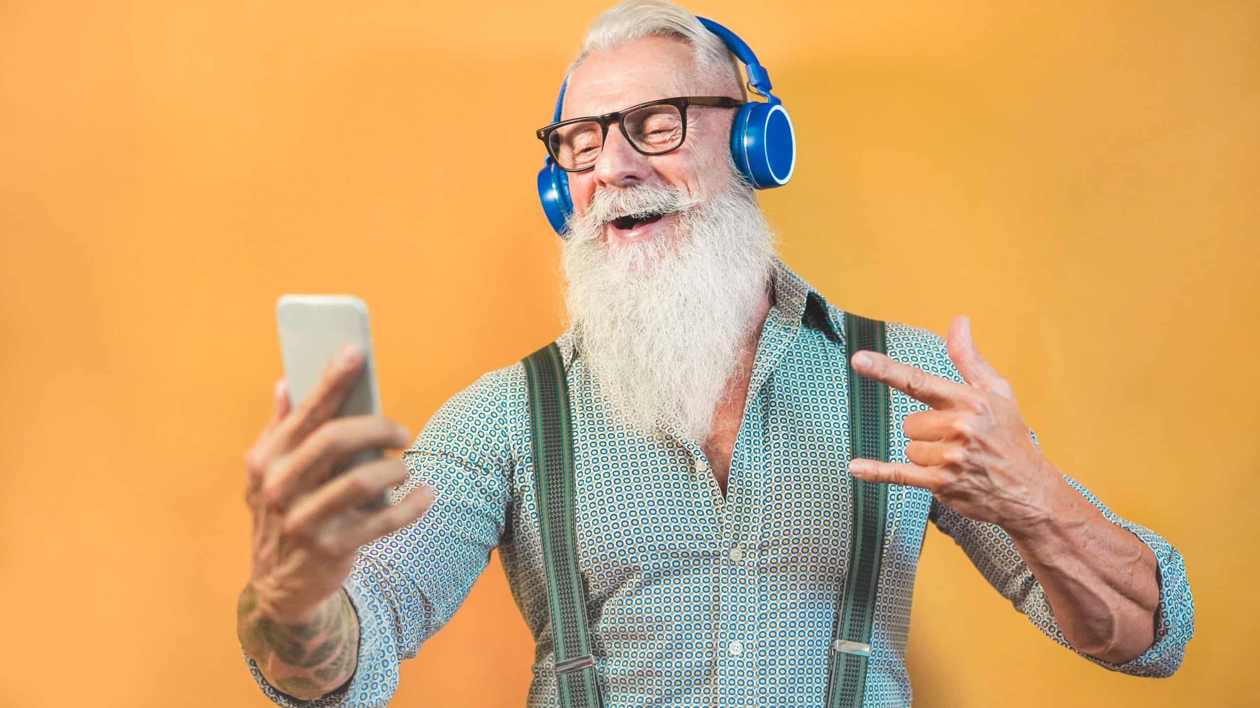 Senior hipster man using smartphone app for creating playlist with rock music - Trendy tattoo guy having fun with mobile phone technology - Tech and joyful elderly lifestyle concept - Focus on face