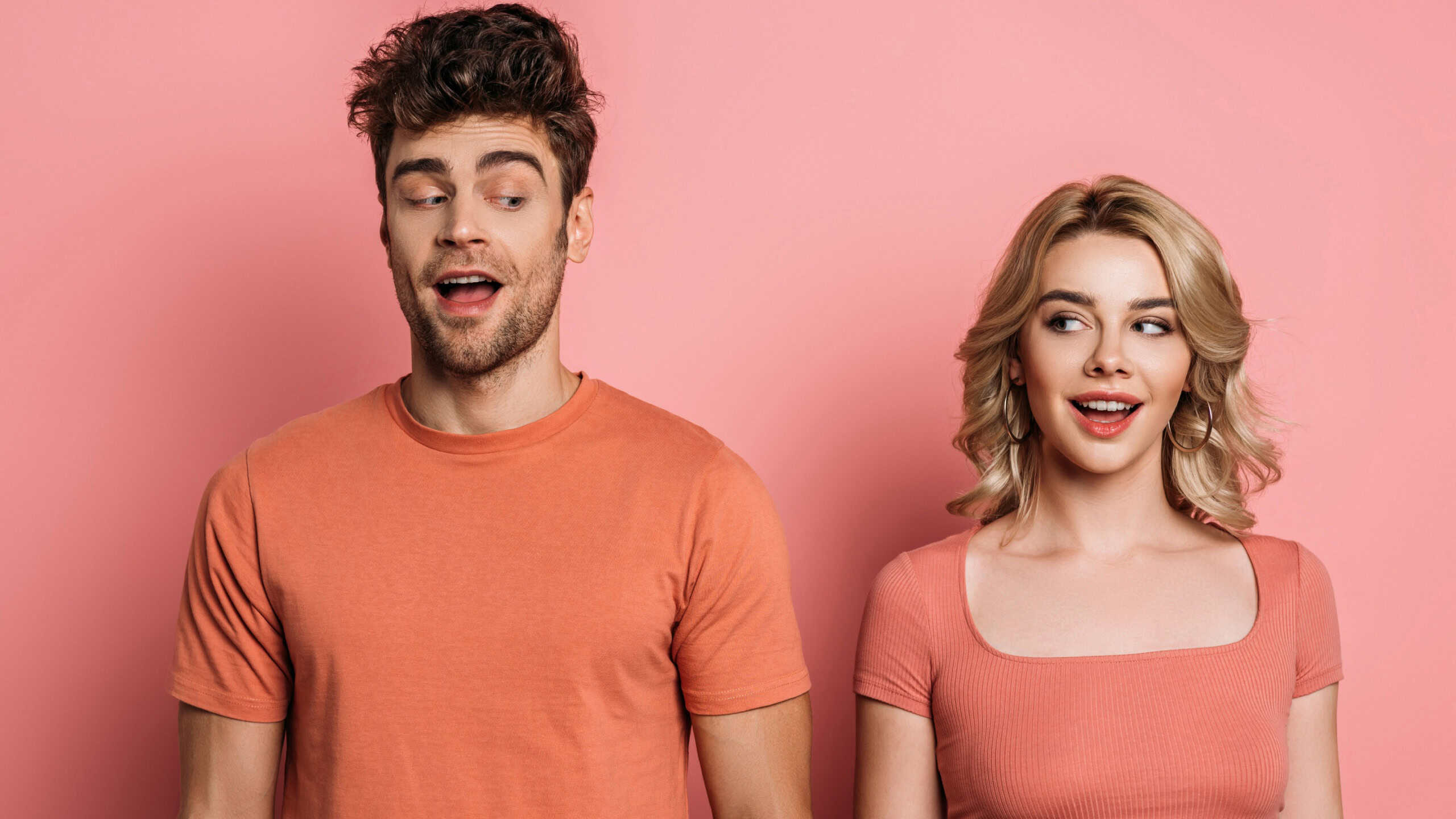positive, tricky man and woman looking at each other on pink background
