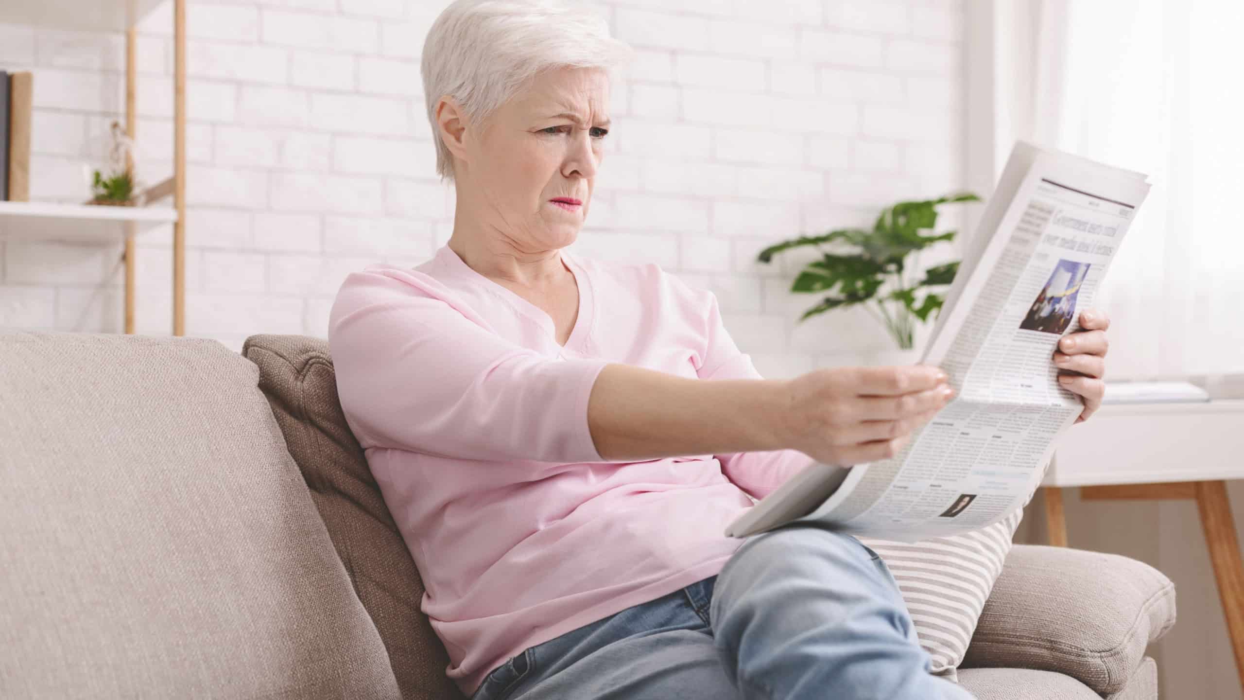 Bad sight problem. Senior lady squinting and holding newspaper far from eyes at home, free space