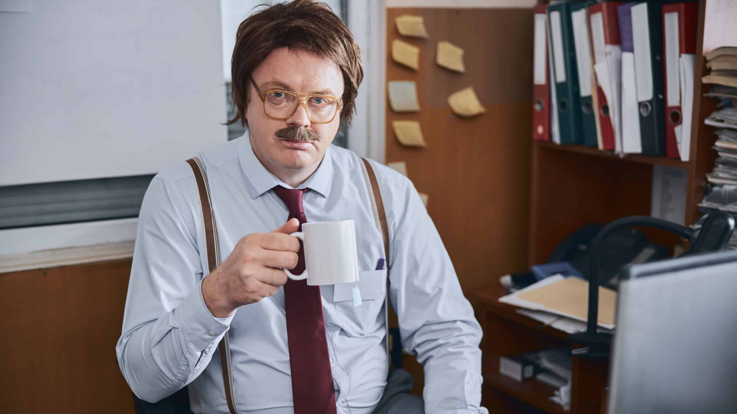 Corpulent manager or accountatnt clothed in old fashioned manner relaxing during break for drink before the screen of his notebook
