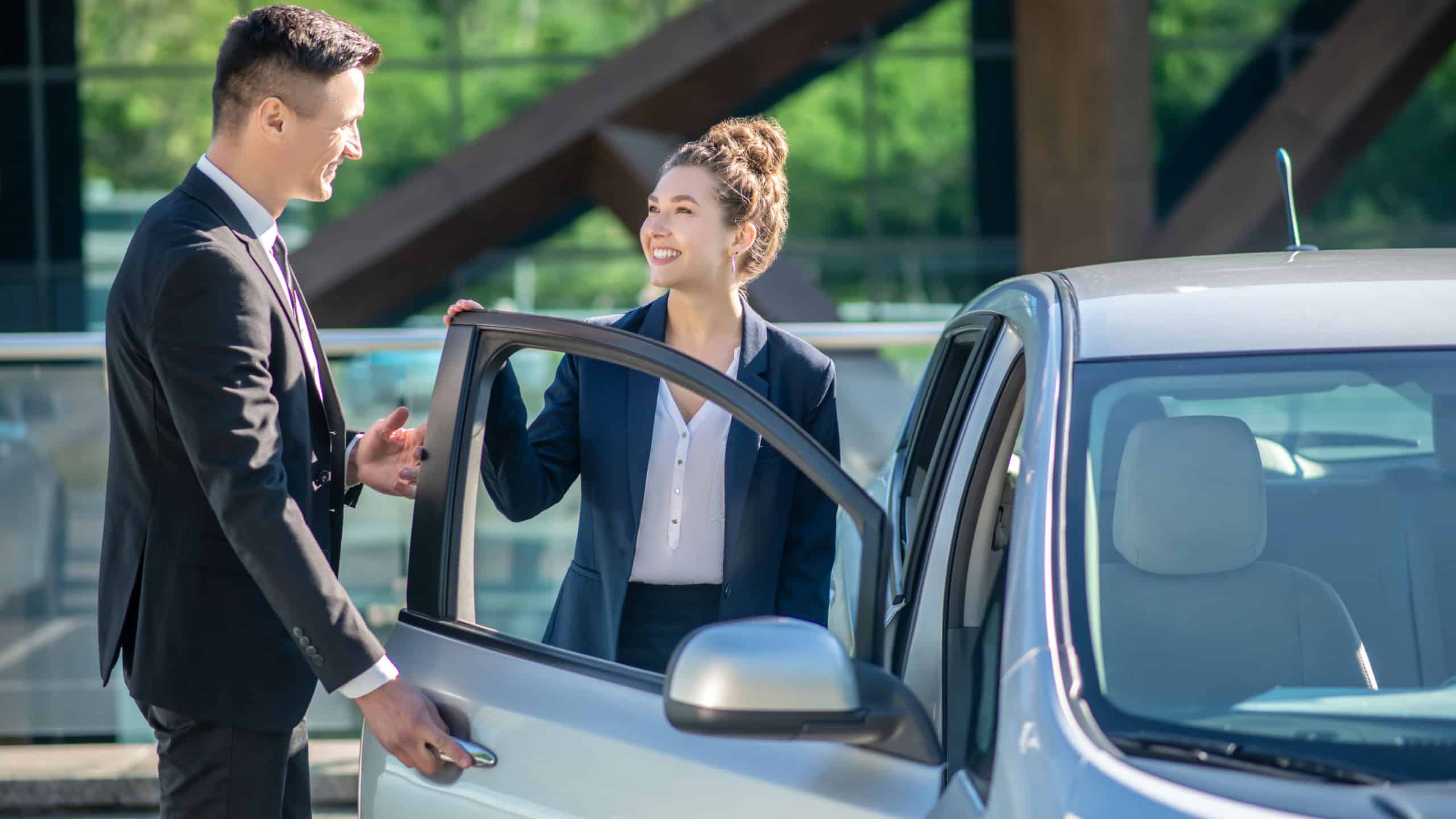 Polite behavior. Polite young man in a suit opening a car door for a pretty smiling woman.