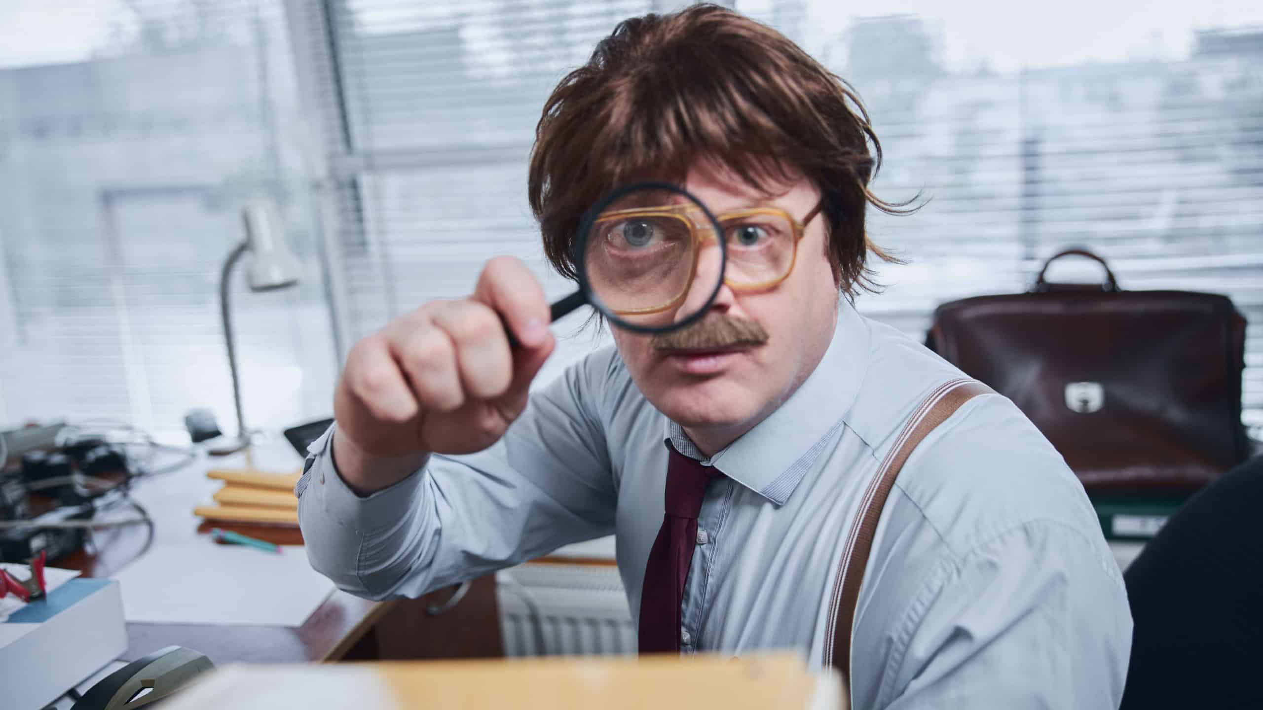 Funny retro bespectacled sheriff feeling curious and looking through the magnifying glass while sitting in the office
