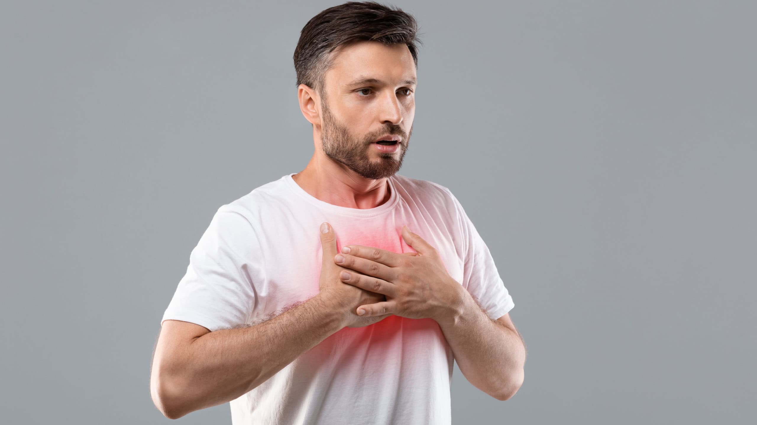 Breathing problem. Sick middle-aged man with chest pain touching inflammated zone and looking at copy space, grey studio background. Bearded man suffering from pneumonia. COVID-19 concept