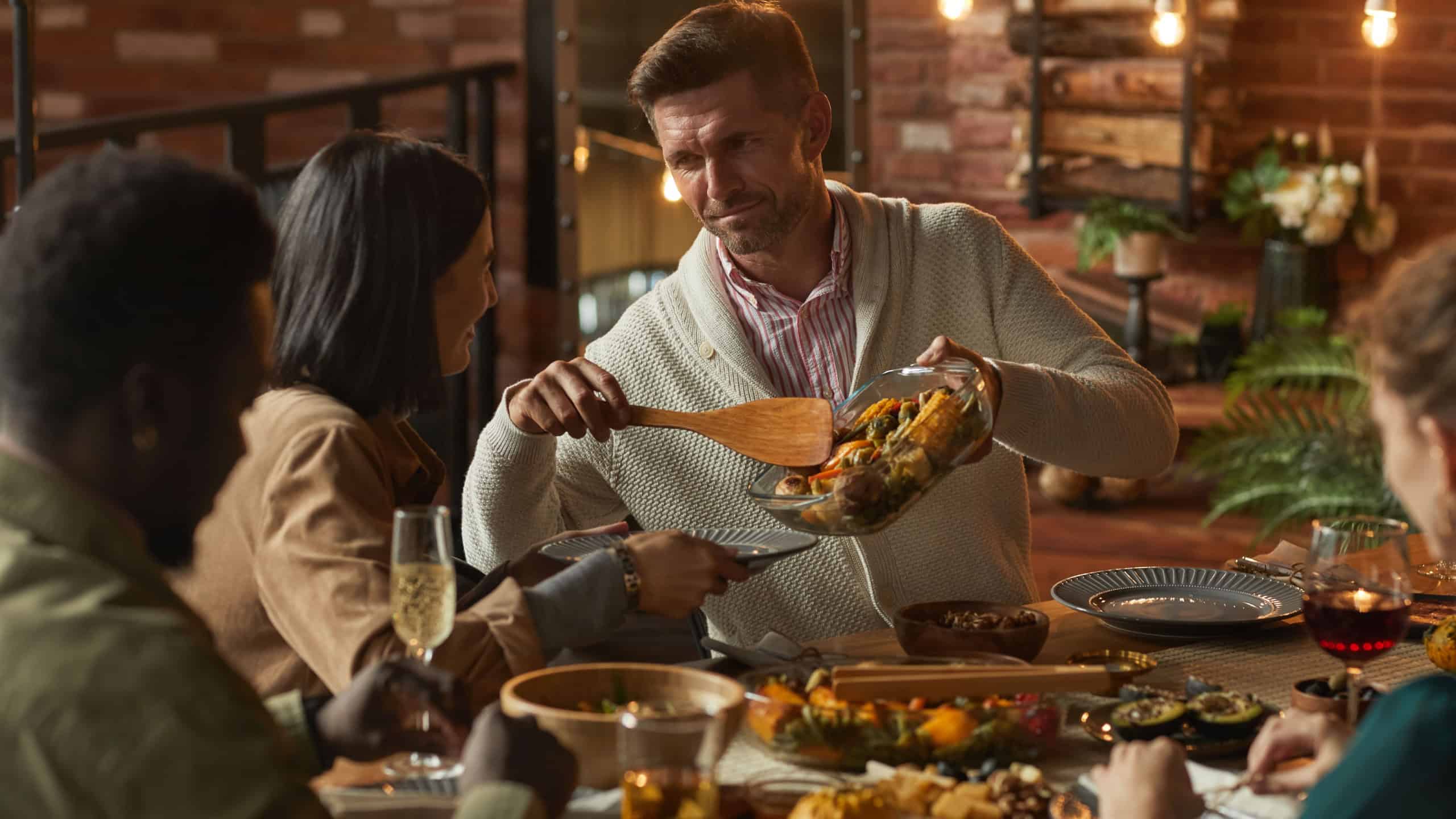 Portrait of handsome mature man serving food while hosting dinner party with friends and family, copy space