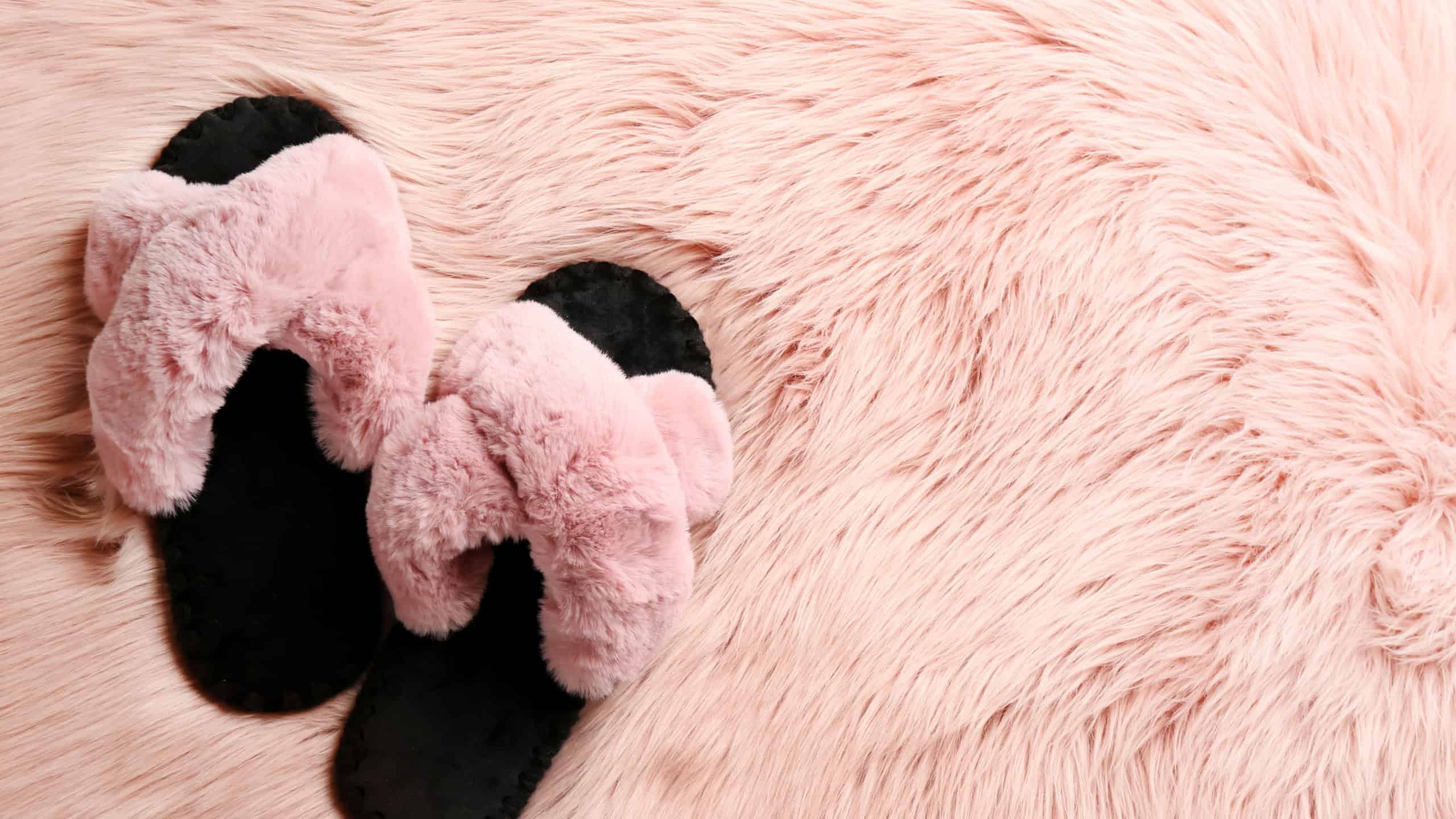 Pair of soft slippers on pink faux fur, flat lay. Space for text