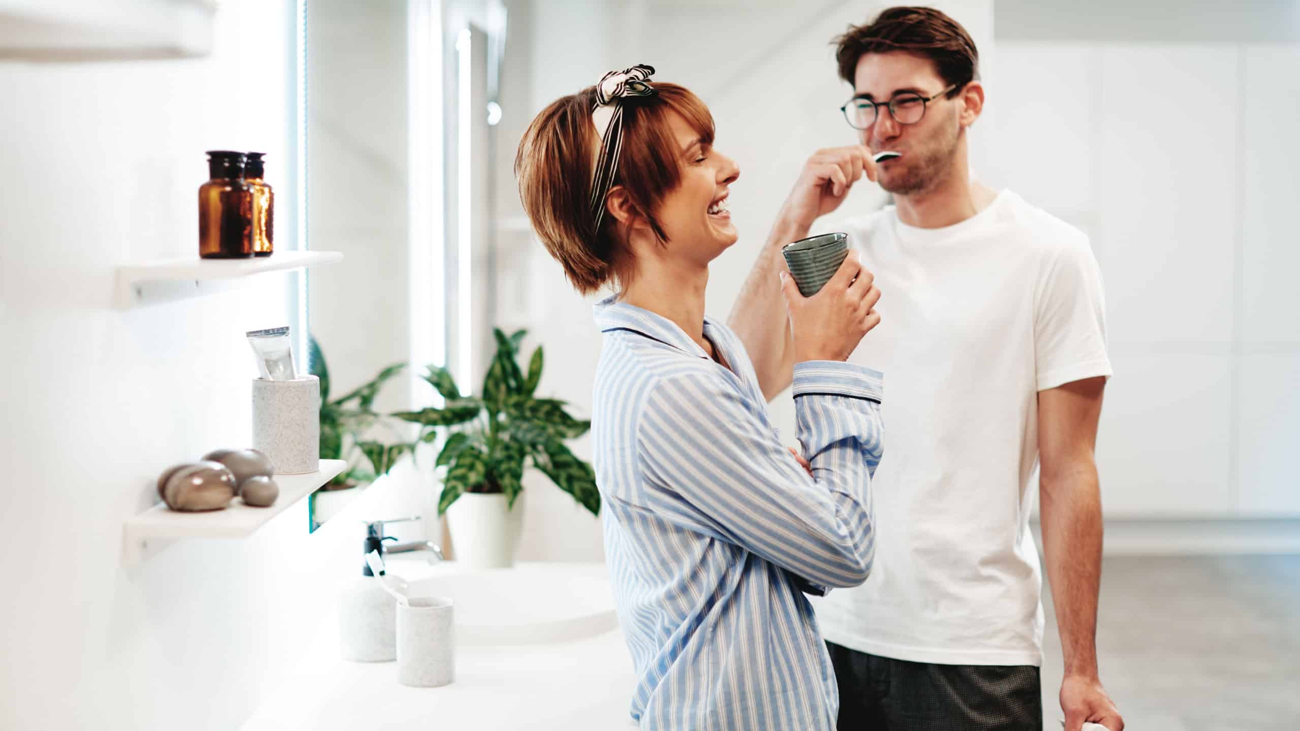 Laughing young couple in pajamas standing together in their bathroom at home and getting ready in the morning
