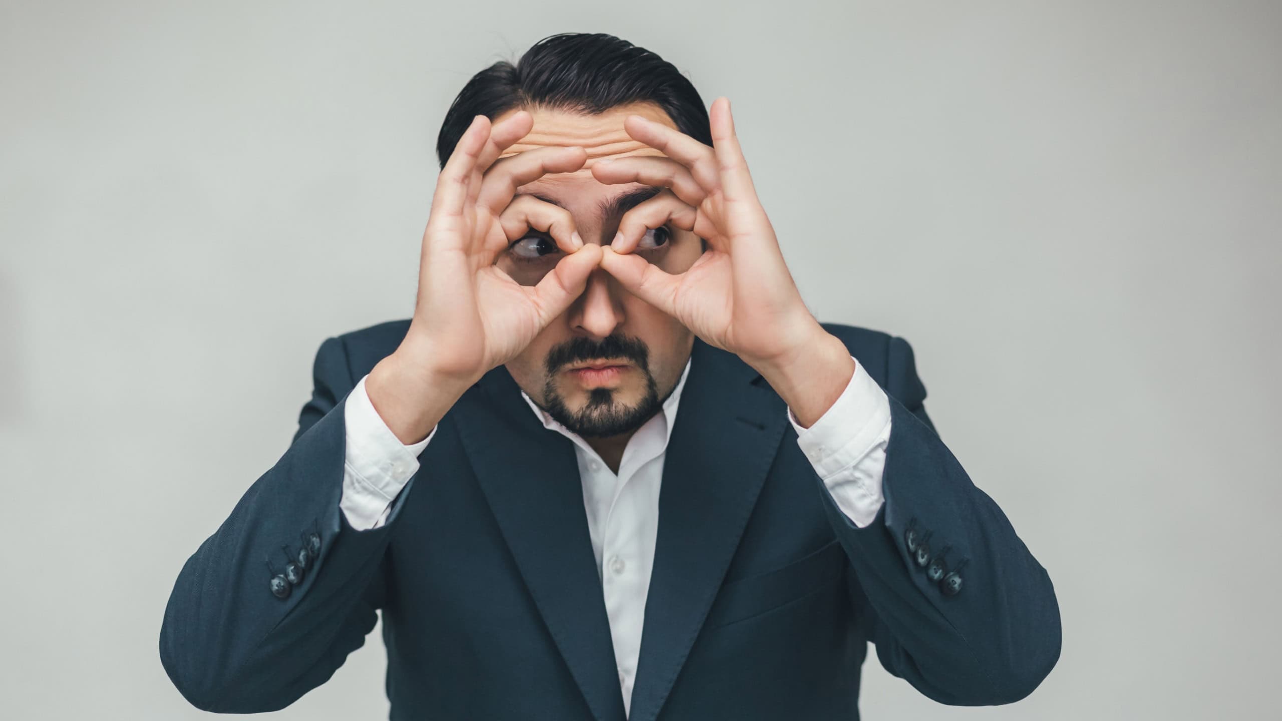 Strange behavior of businessman keeping hands like binocular and looking suspiciously at something.