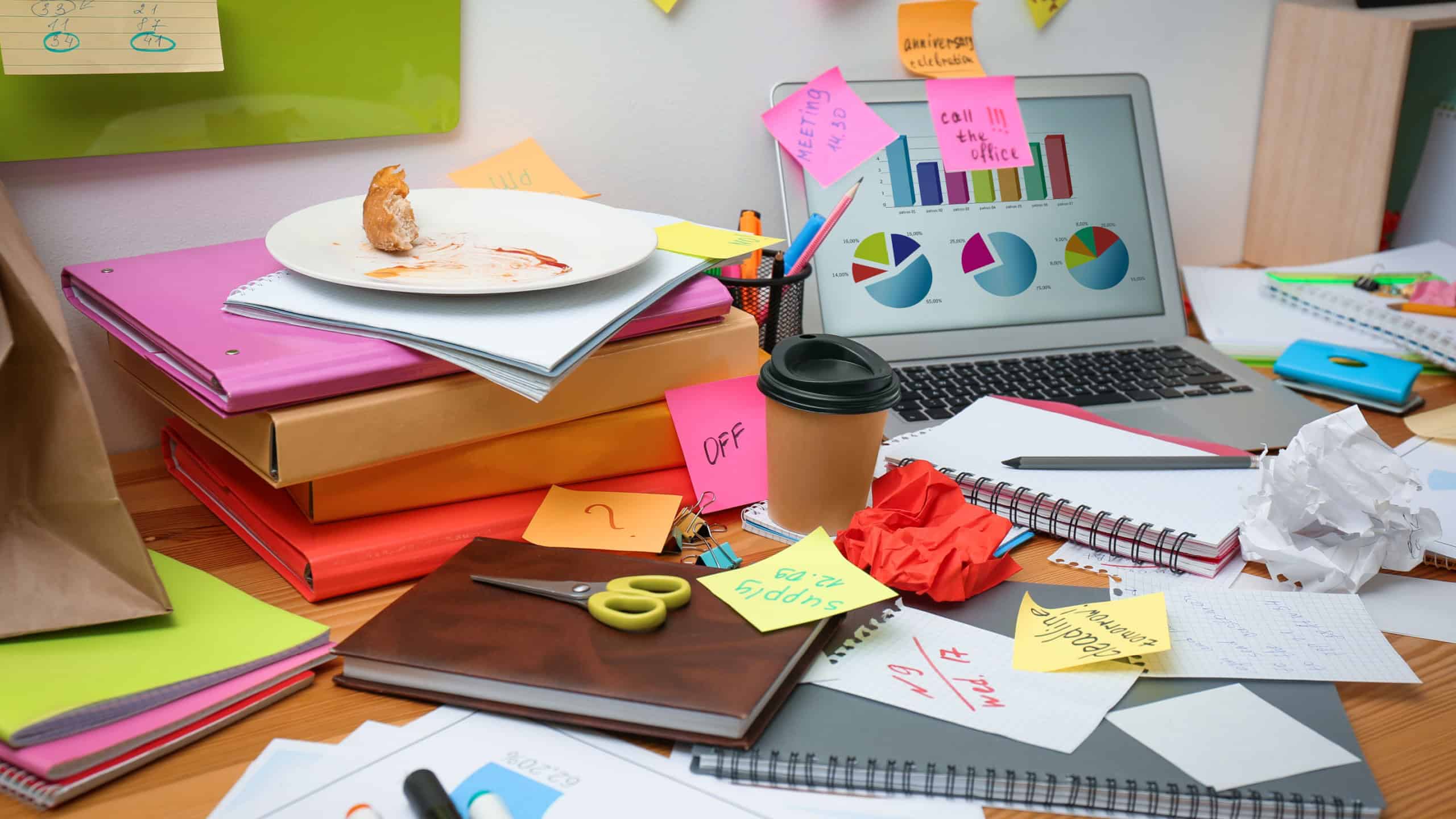 Messy table with laptop and stationery. Concept of being overwhelmed by work