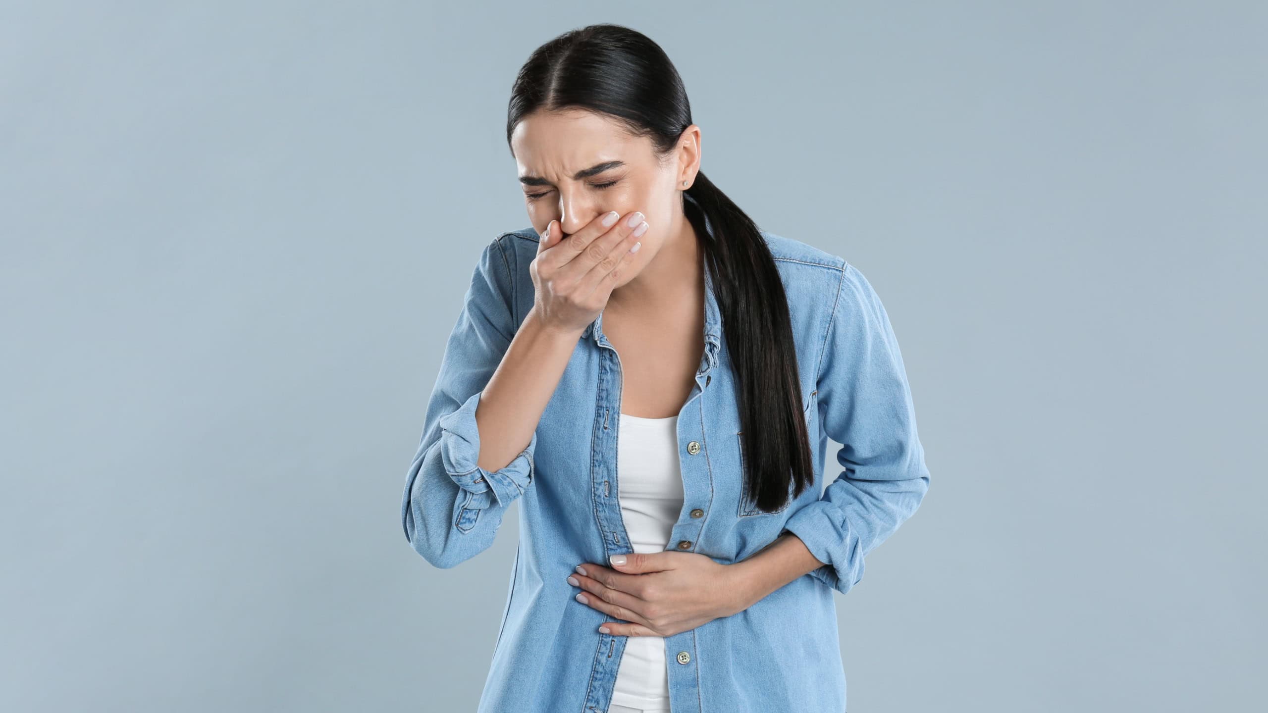 Woman suffering from stomach ache and nausea on grey background. Food poisoning