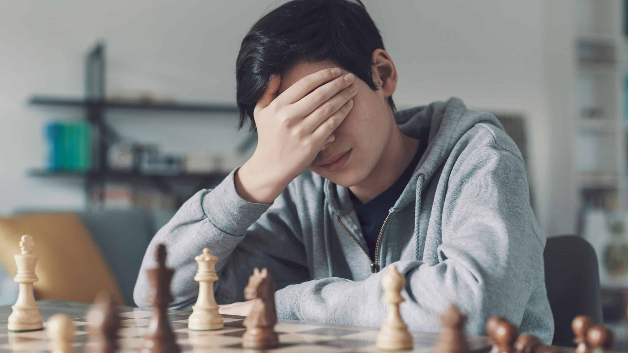 Boy playing chess and losing the game, he is disappointed and covering his face with the hand