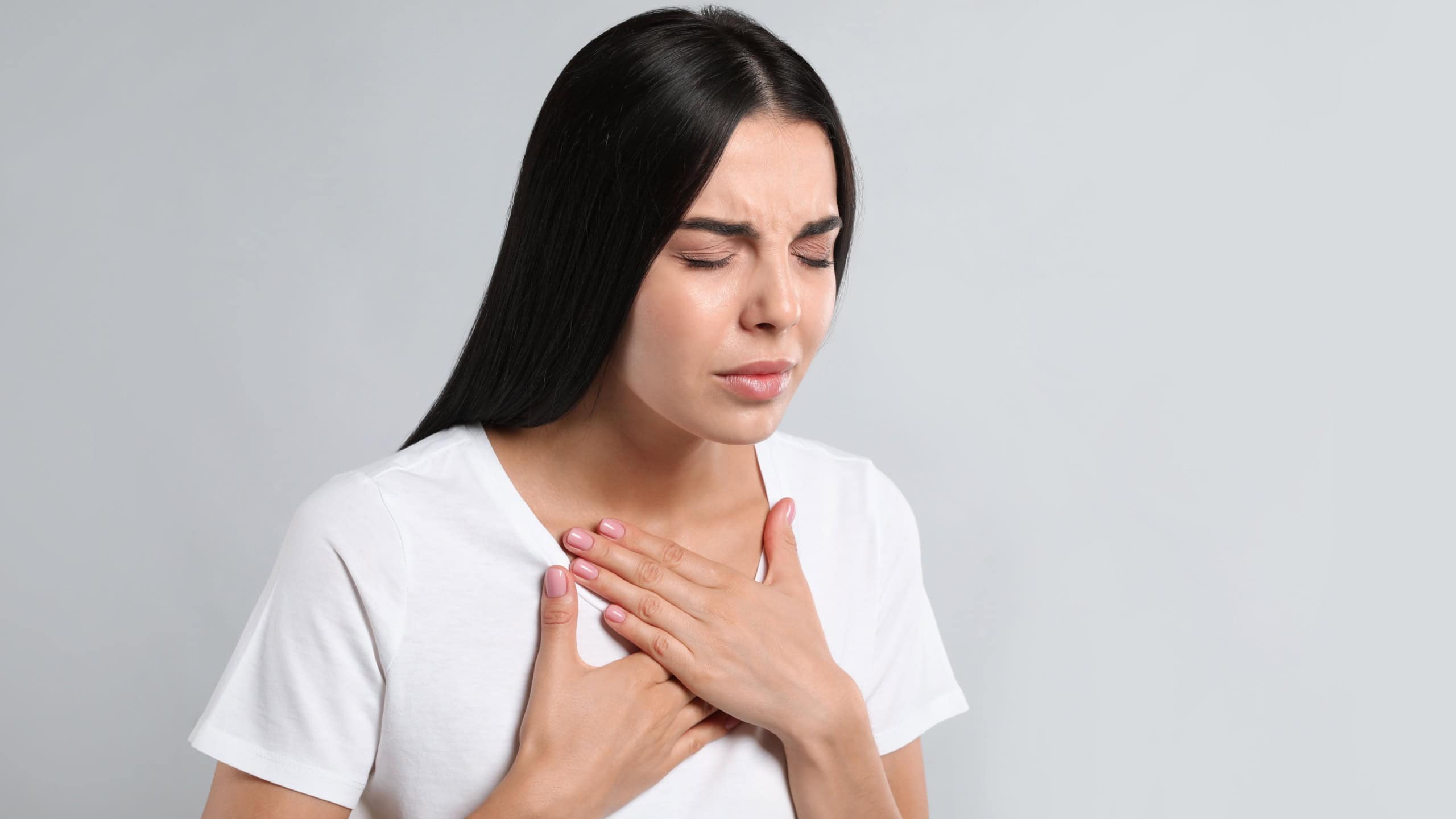 Young woman suffering from breathing problem on light background