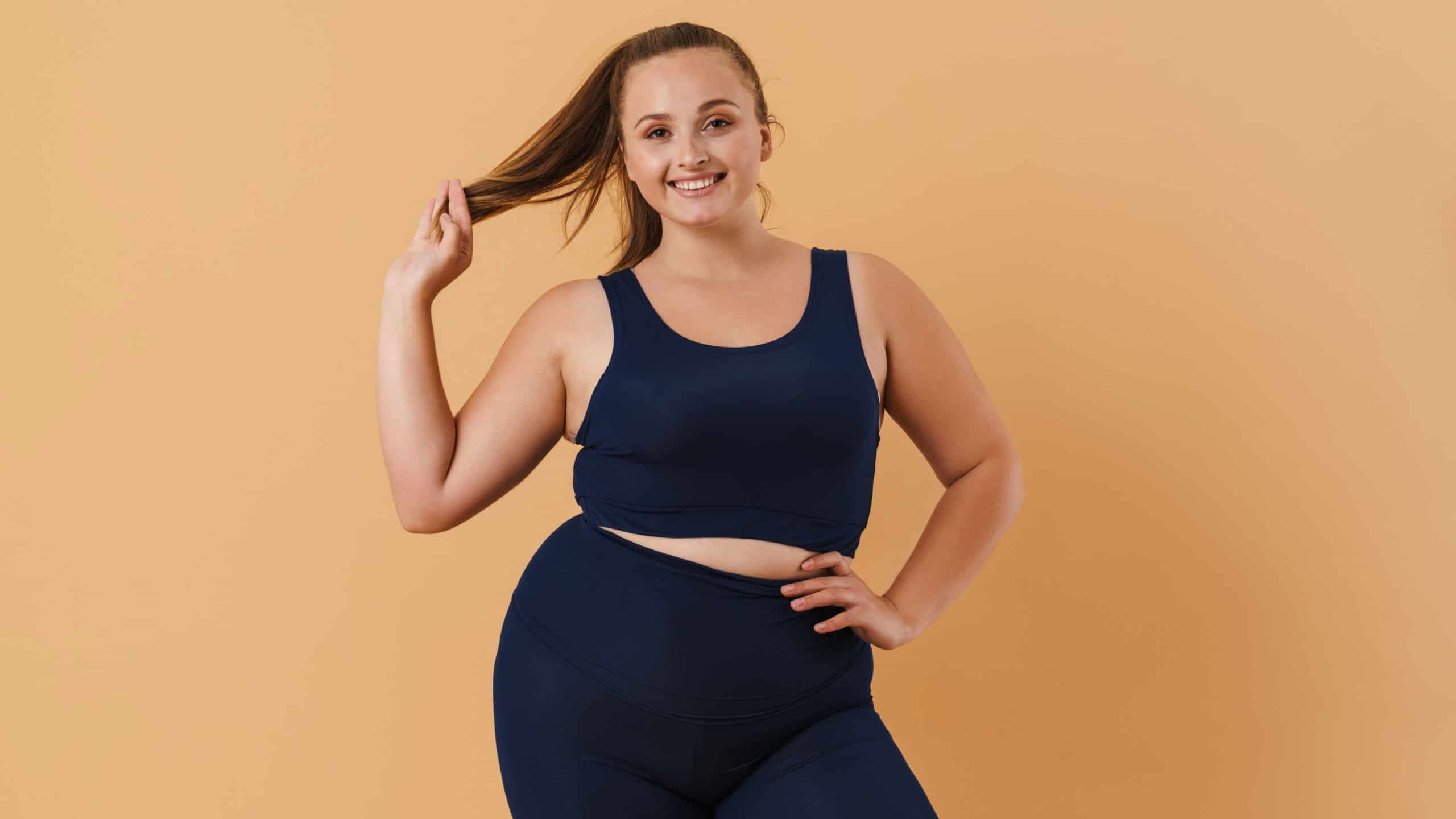 Young woman wearing sport suit smiling and looking at camera isolated over beige background