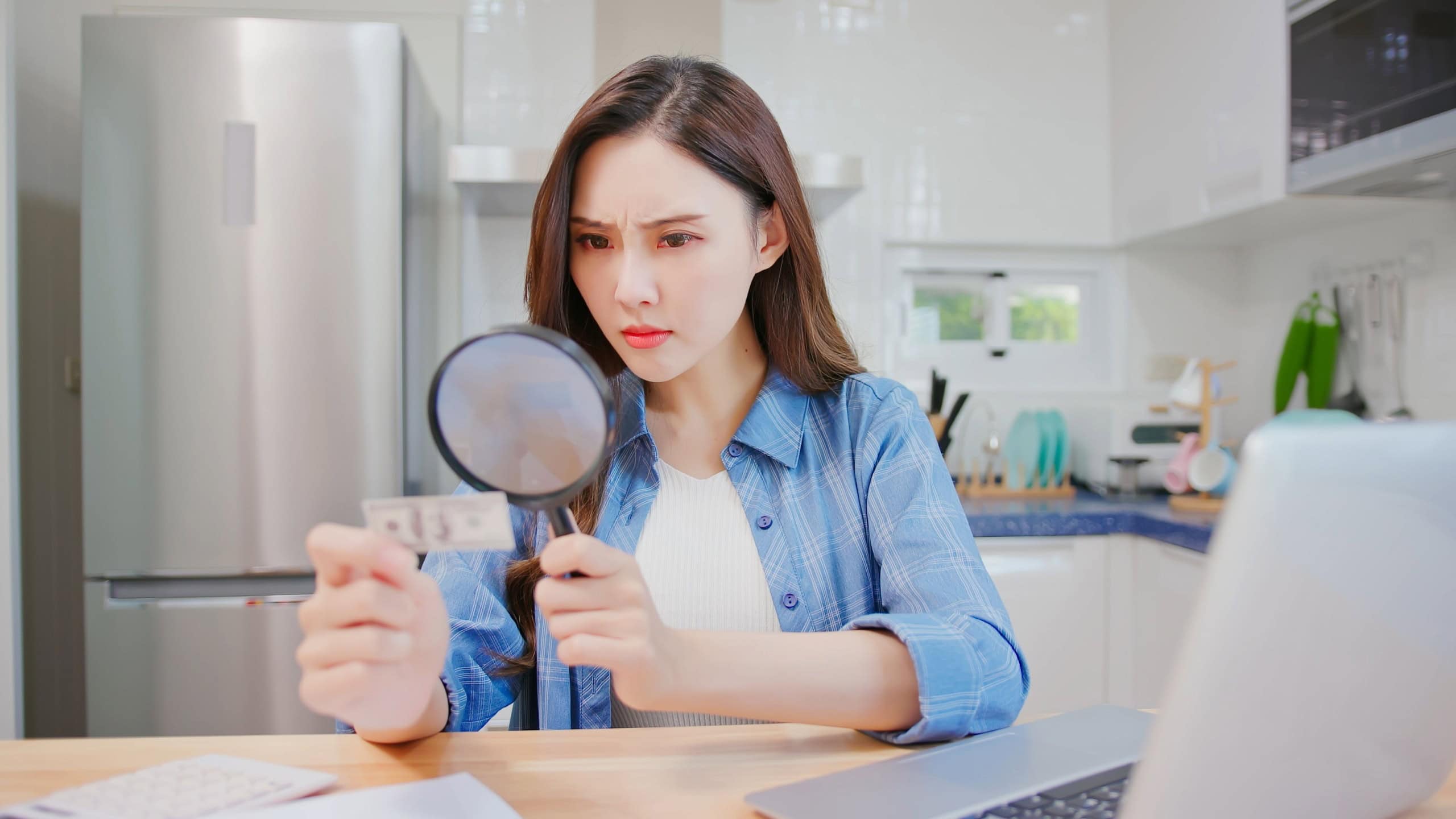 inflation concept - worried asian woman find money is getting smaller by magnifier at kitchen