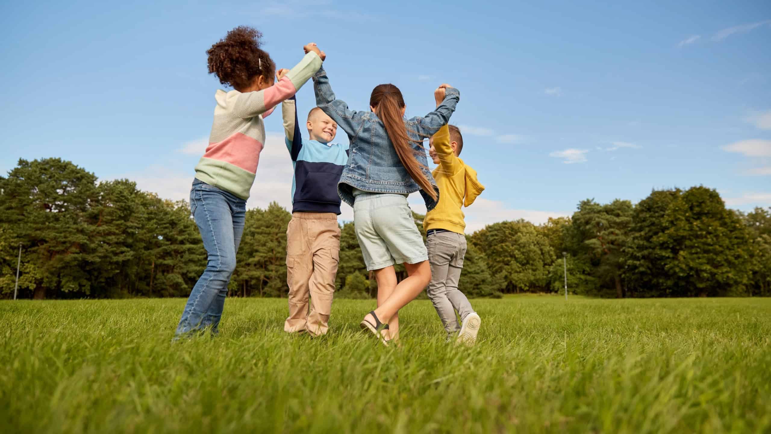 childhood, leisure and people concept - group of happy kids playing round dance at park