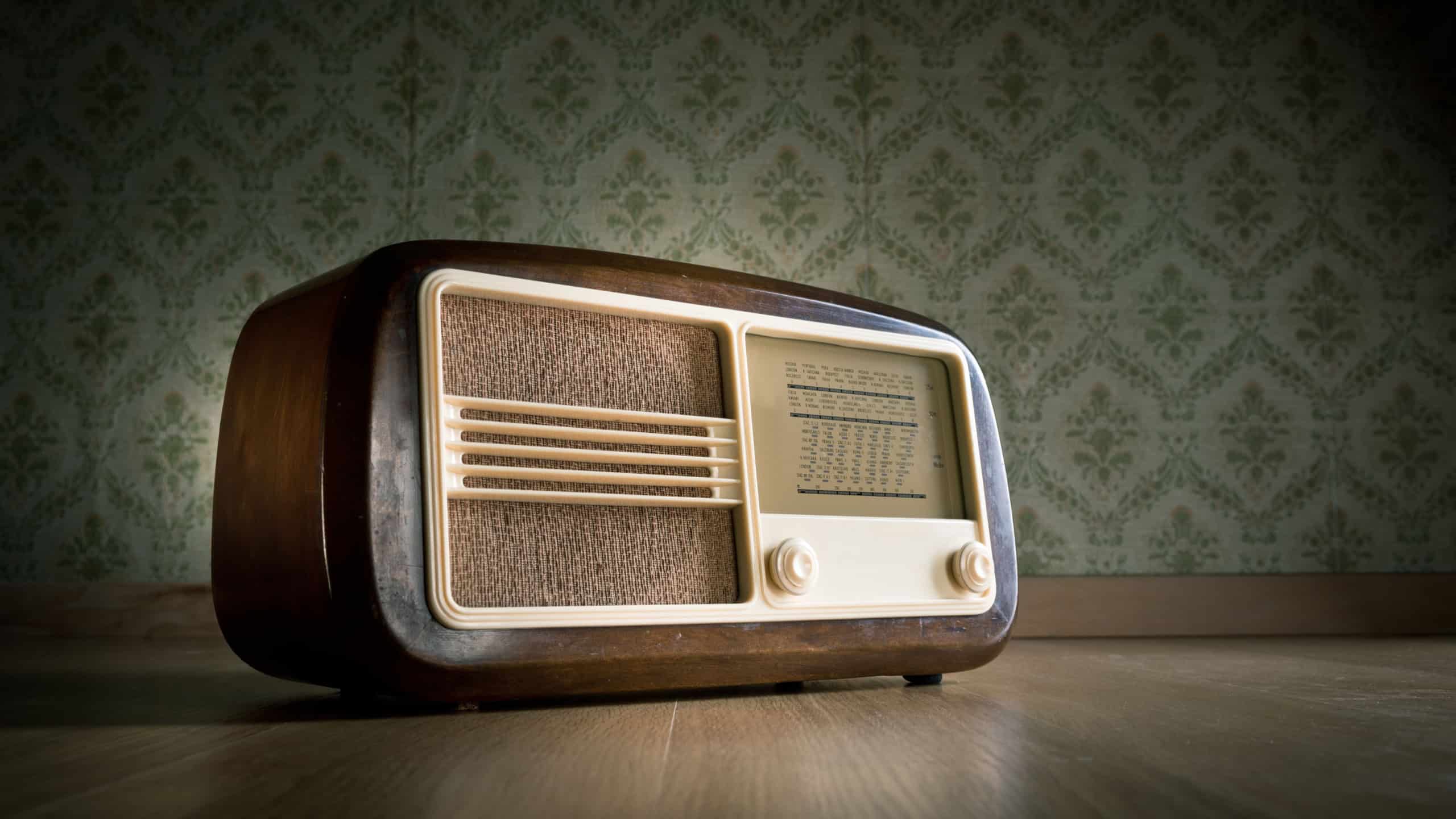 Old vintage radio on hardwood floor with retro wallpaper on background.