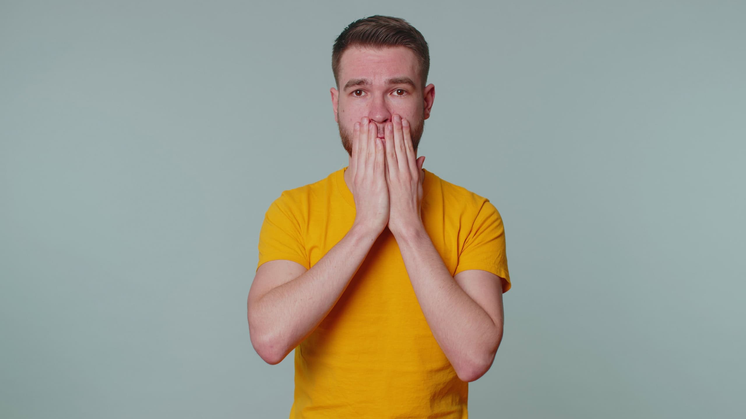 I will not say anyone. Frightened sincere man closing his mouth with hand, looking intimidated scared at camera, gestures no, refusing to tell terrible secret, unbelievable truth. Afraid young one guy
