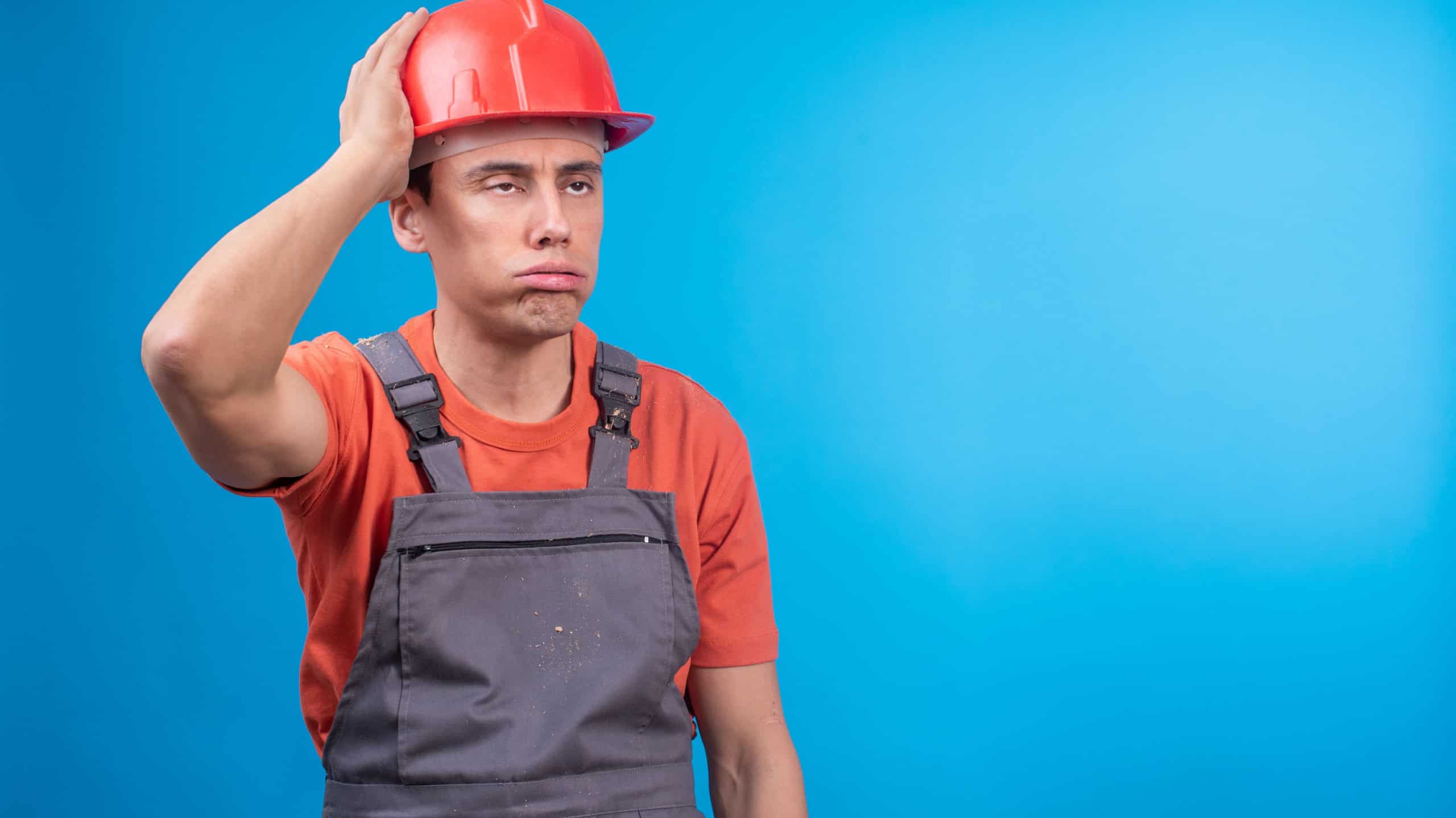 Tired male builder in uniform touching hardhat