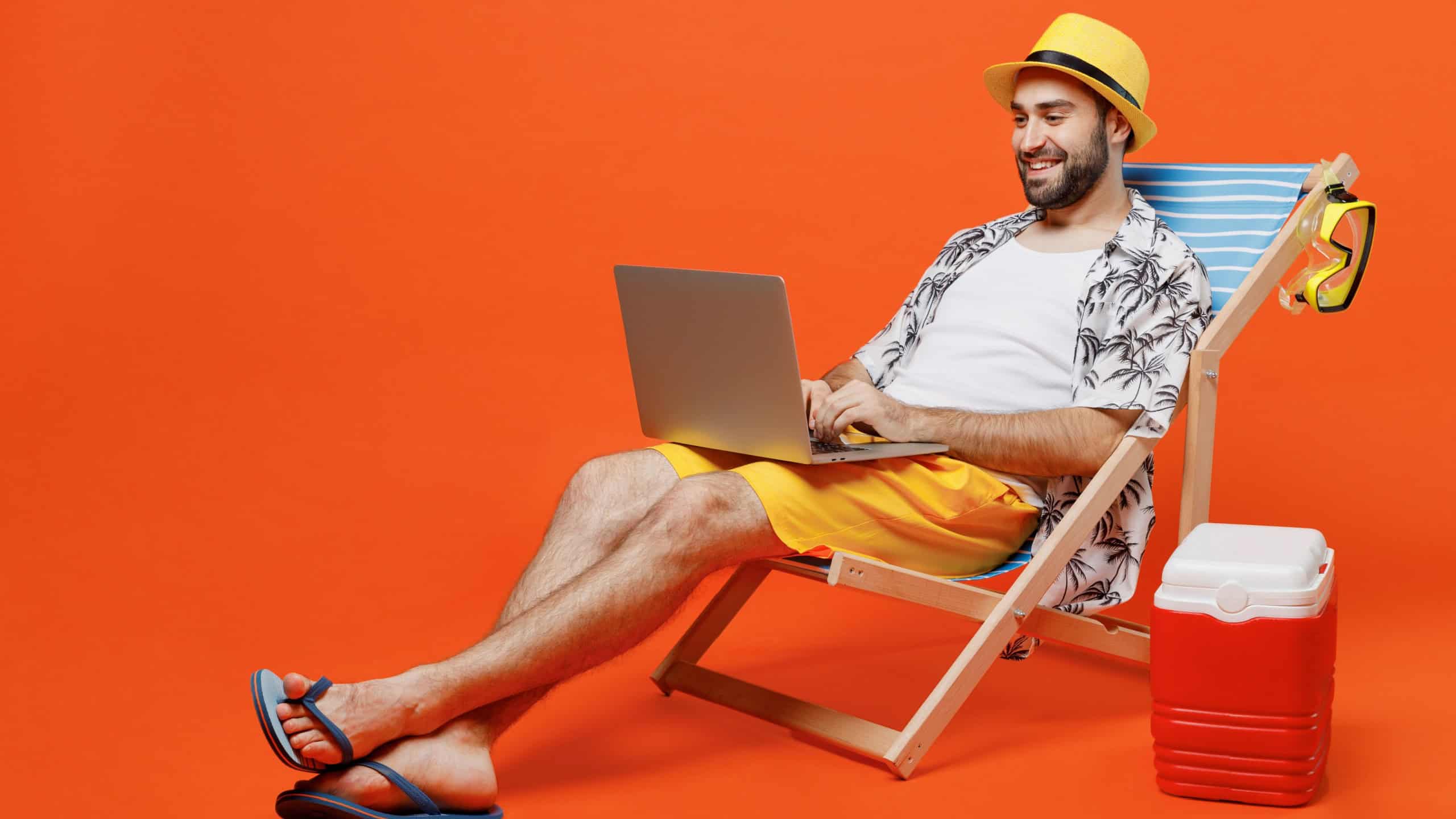 Young fun happy tourist man 20s wear beach shirt hat lie on deckchair hold use work on laptop pc computer isolated on plain orange background studio portrait. Summer vacation sea rest sun tan concept.