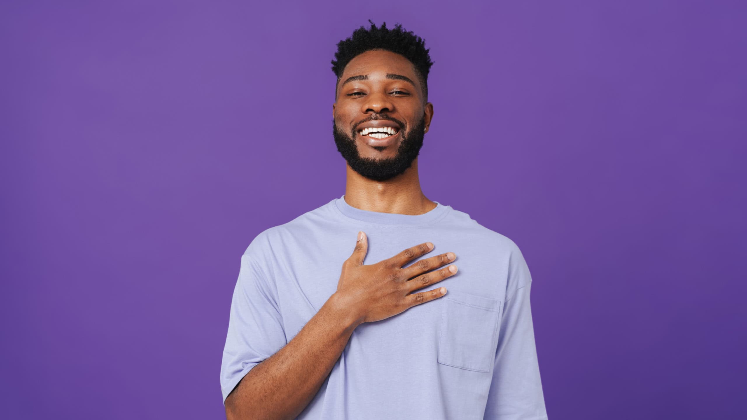 Black bearded man wearing t-shirt laughing while holding his chest isolated over purple background