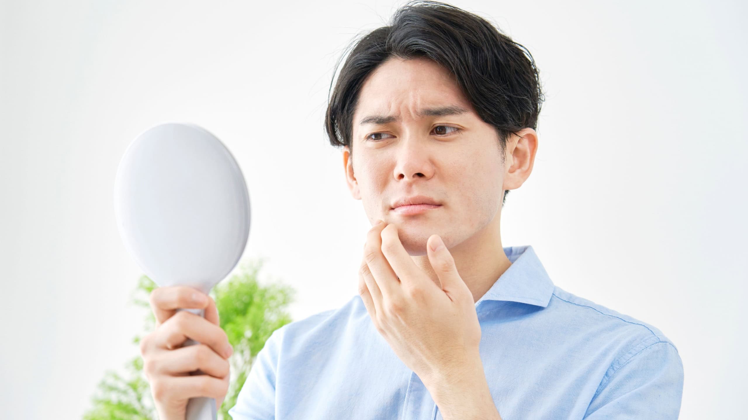 Asian man checking his face skin with the mirror