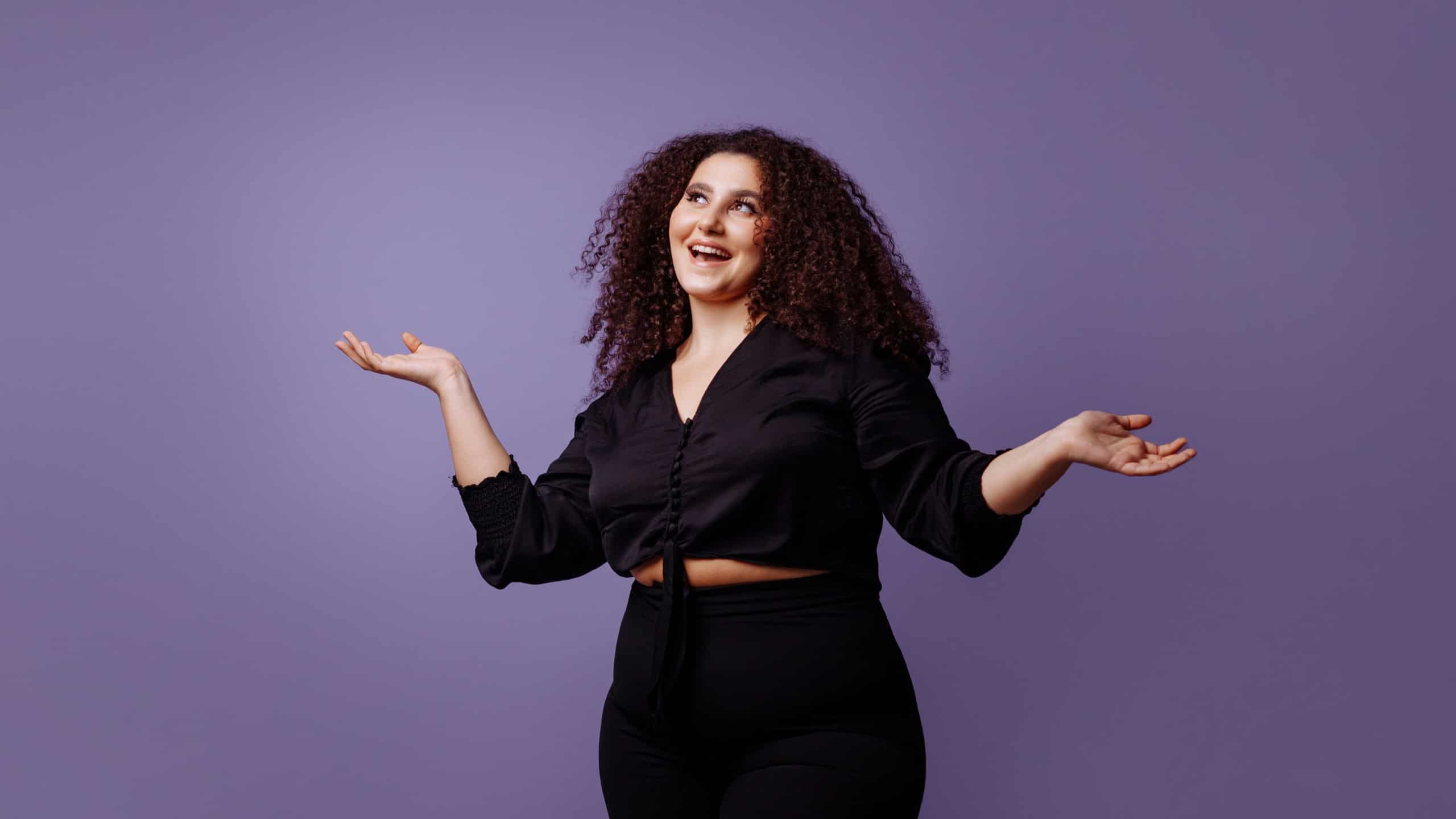 Attractive stylish plus size woman model with curly cool hairstyle in dark clothes on lilac background.