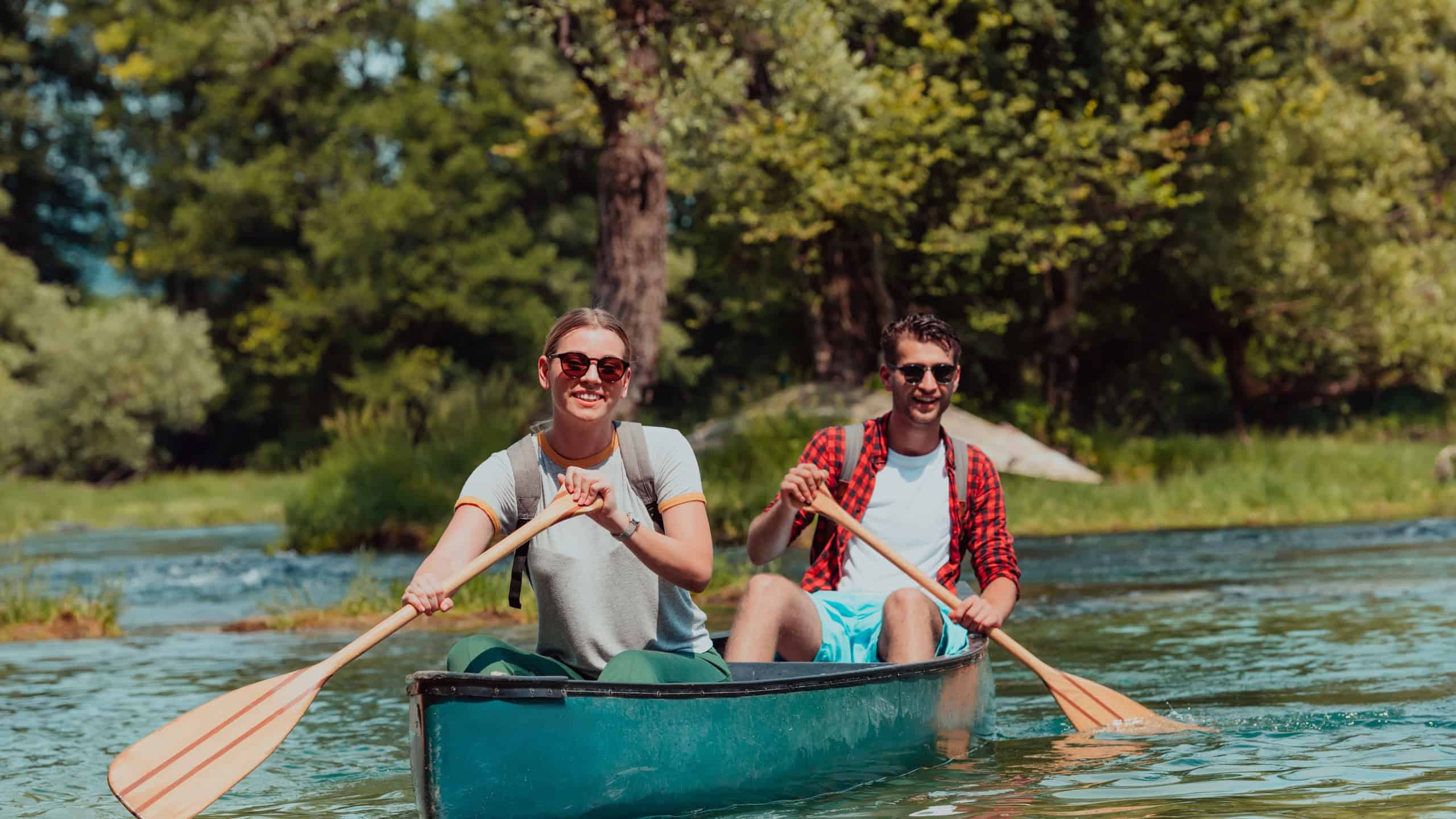 Couple adventurous explorer friends are canoeing in a wild river surrounded by the beautiful nature