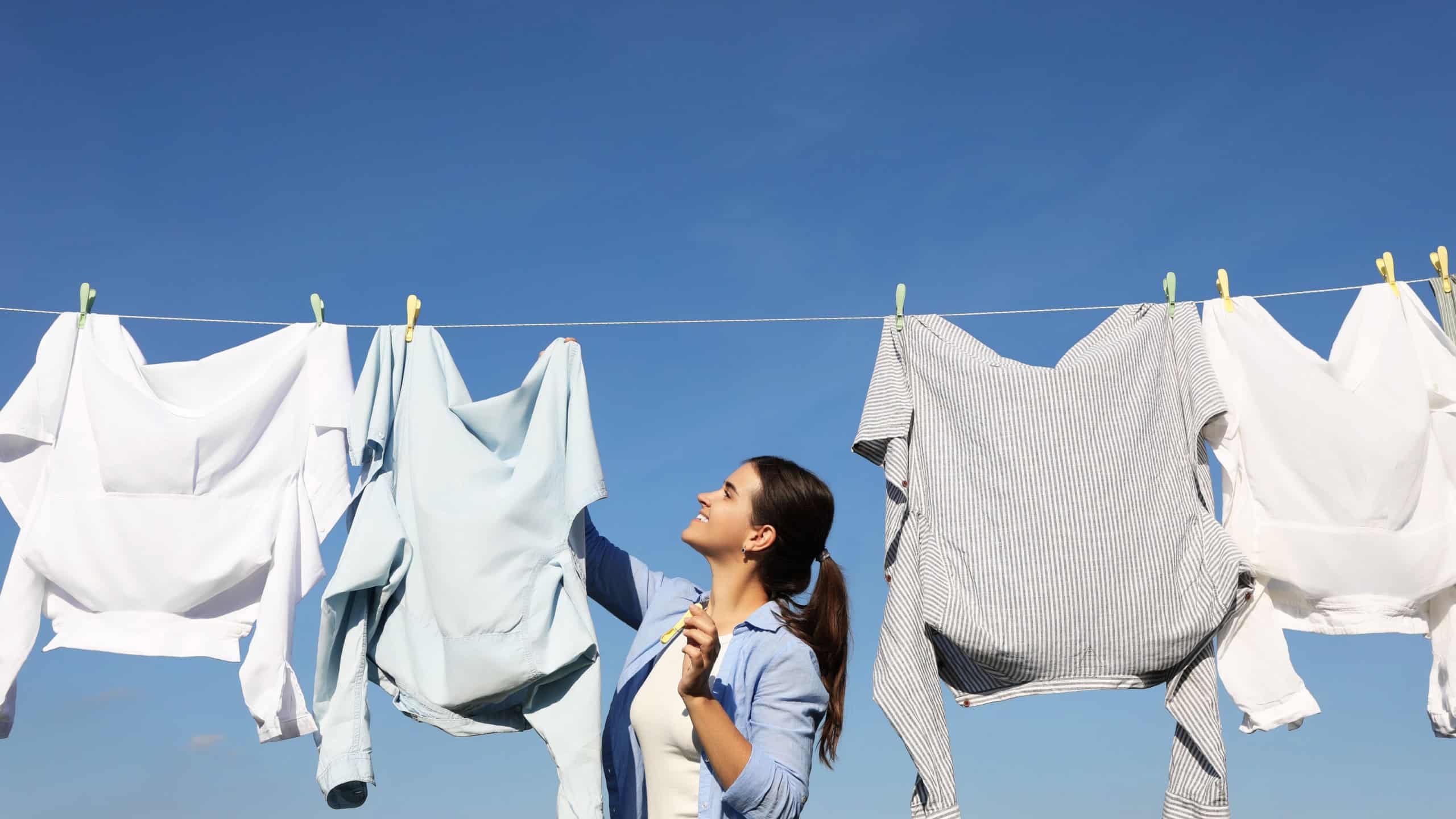Woman hanging clothes with clothespins on washing line for drying against blue sky