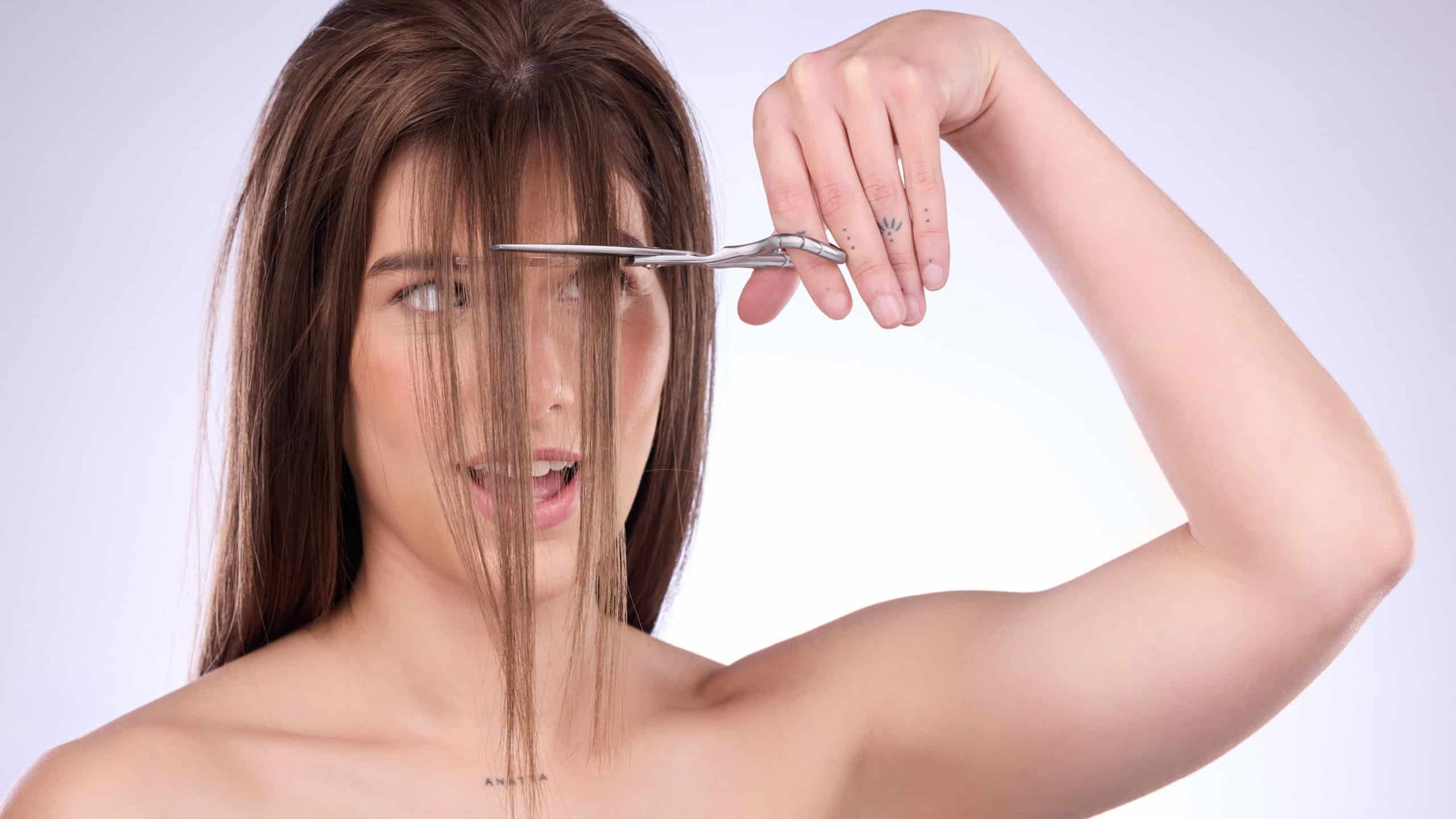 Beauty, salon and a woman self cutting her hair in studio on a gray background for style or care. Grooming, shampoo and haircut with an attractive young female trimming her bangs for haircare