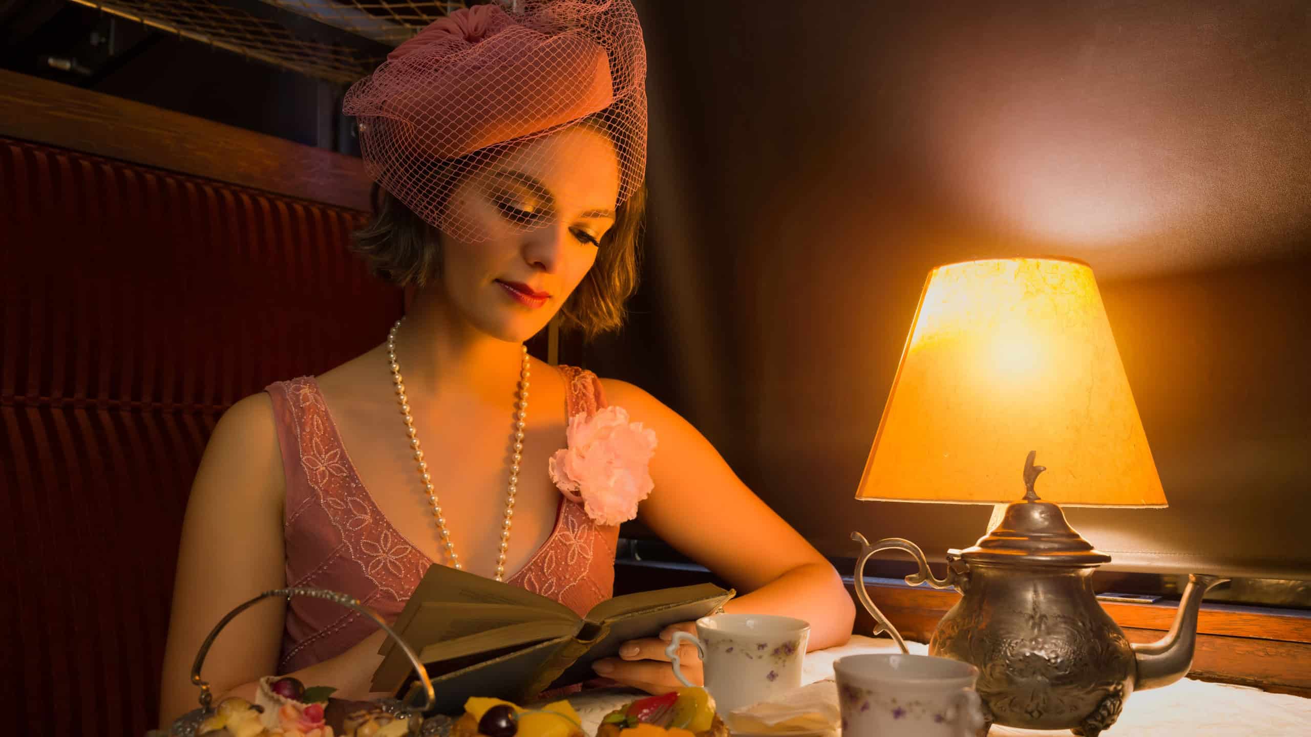 Reenactment scene of a 1920s flapper dress lady enjoying high tea in an authentic 1927 steam train compartment