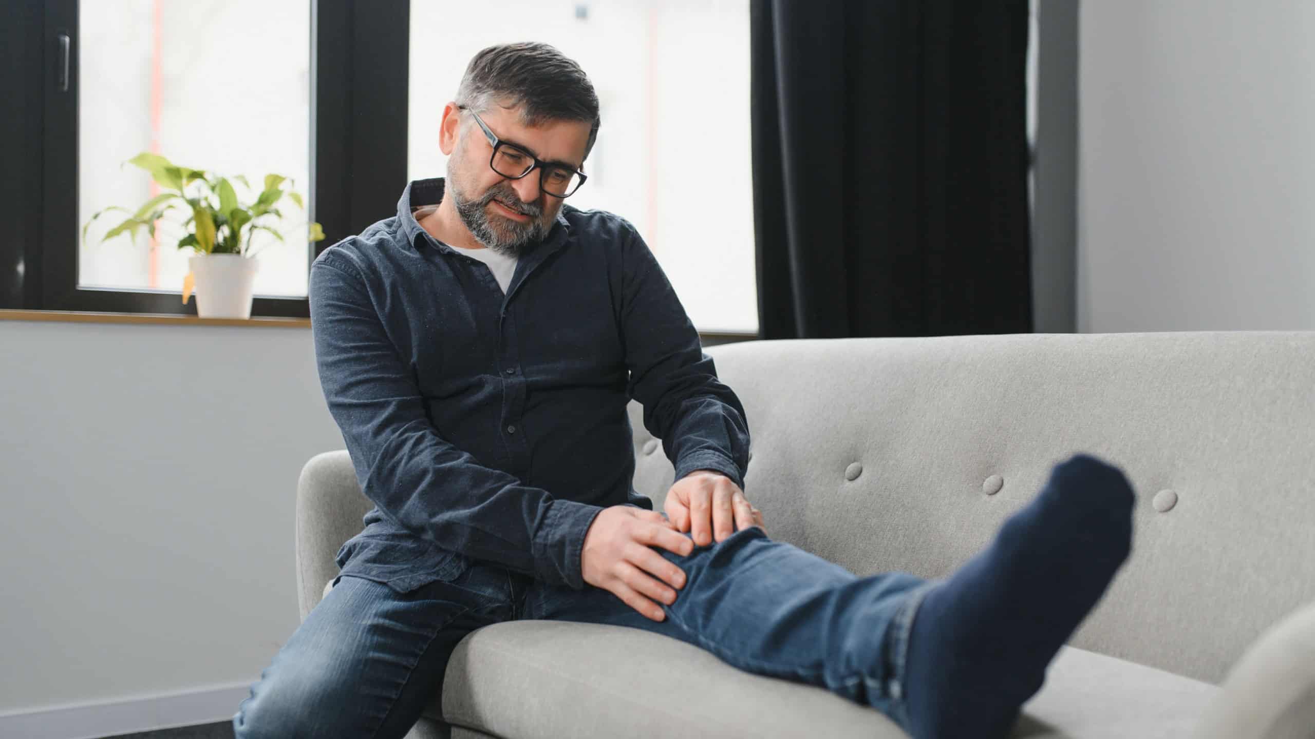 people, health care and problem concept - unhappy senior man suffering from knee ache at home.