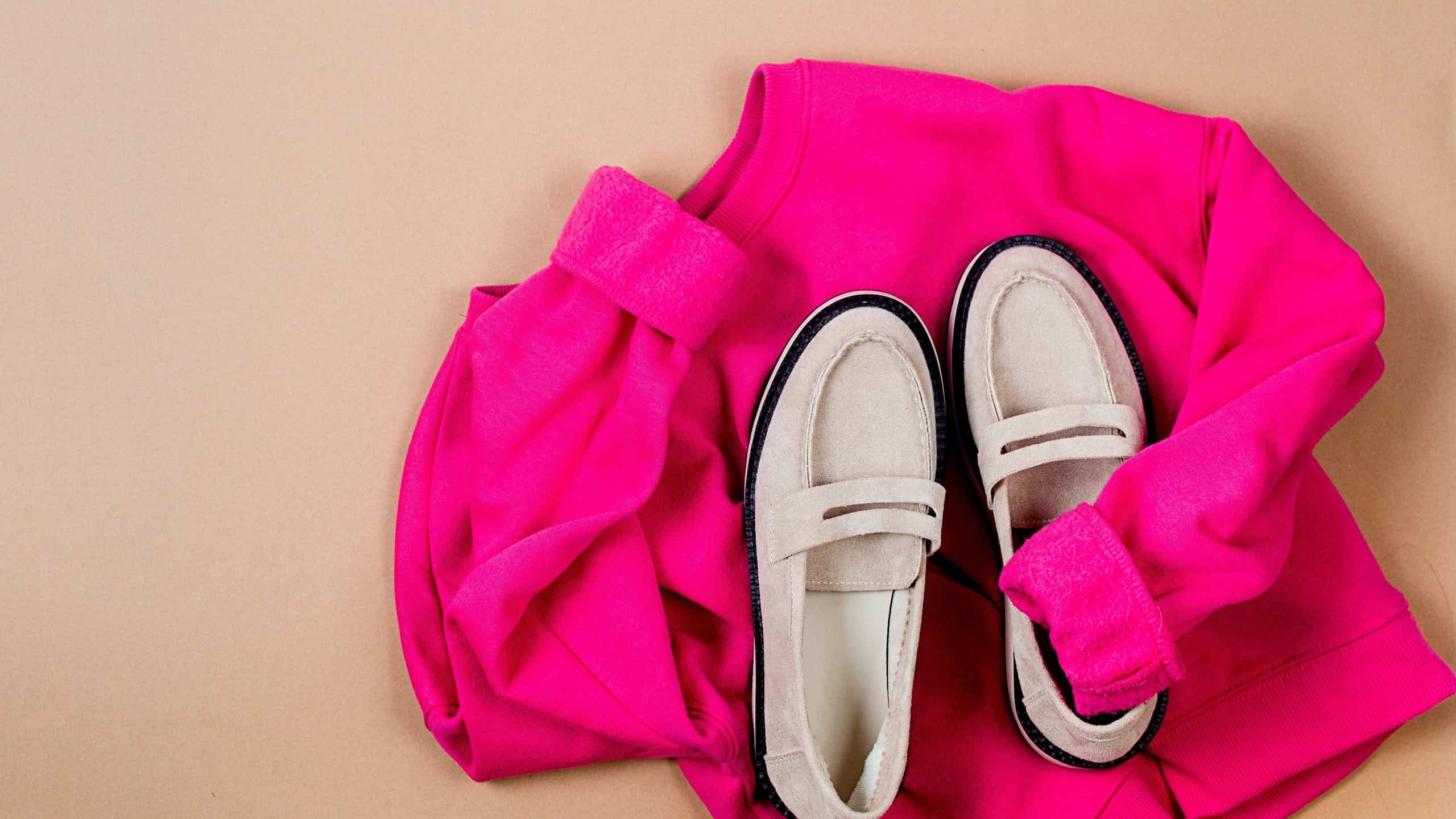 Pink sweatshirt and beige suede loafers on beige background. Overhead view of women's casual day outfit. Trendy women clothes. 
