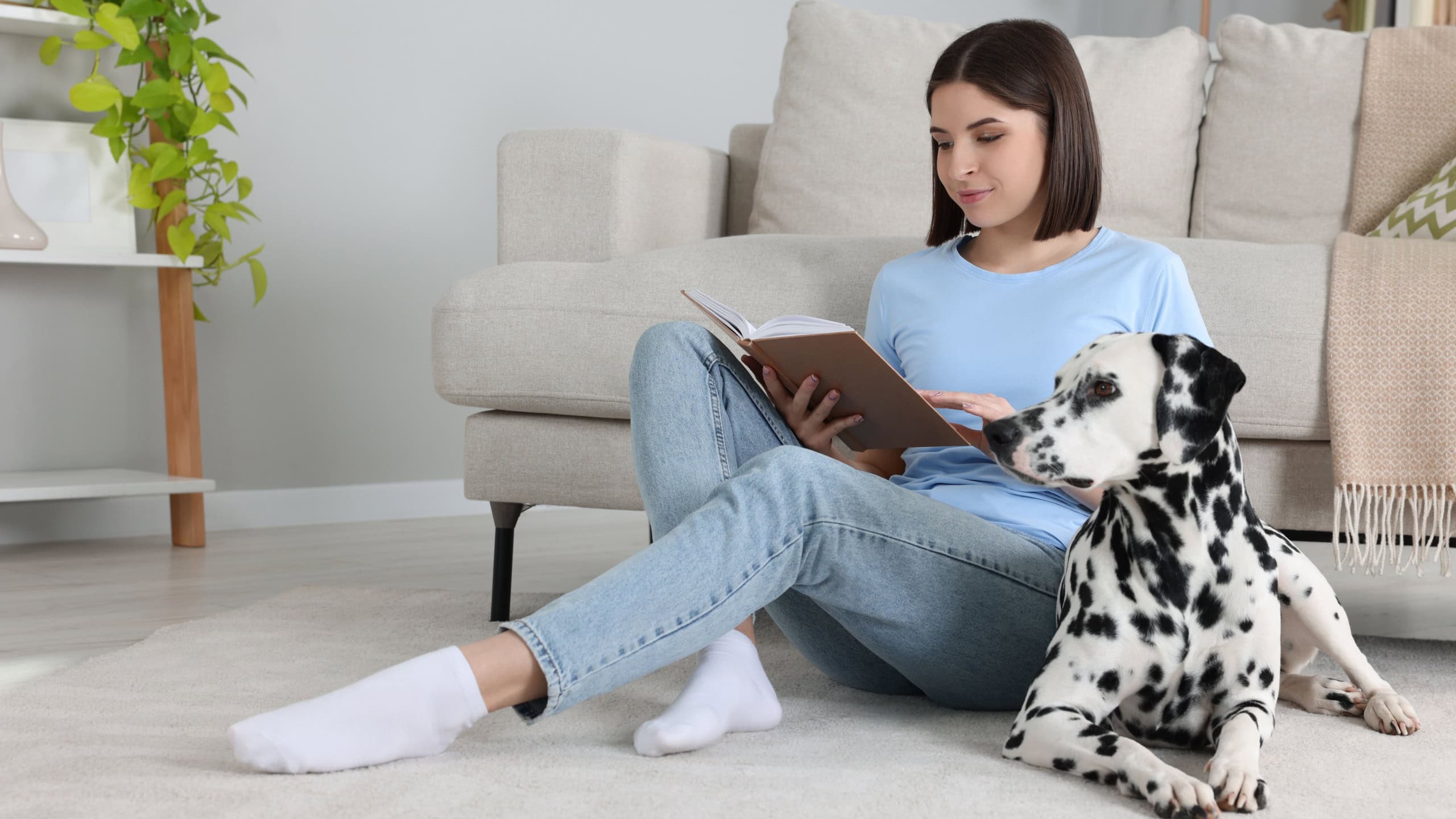 Beautiful young woman reading book and her adorable Dalmatian dog on floor at home. Lovely pet