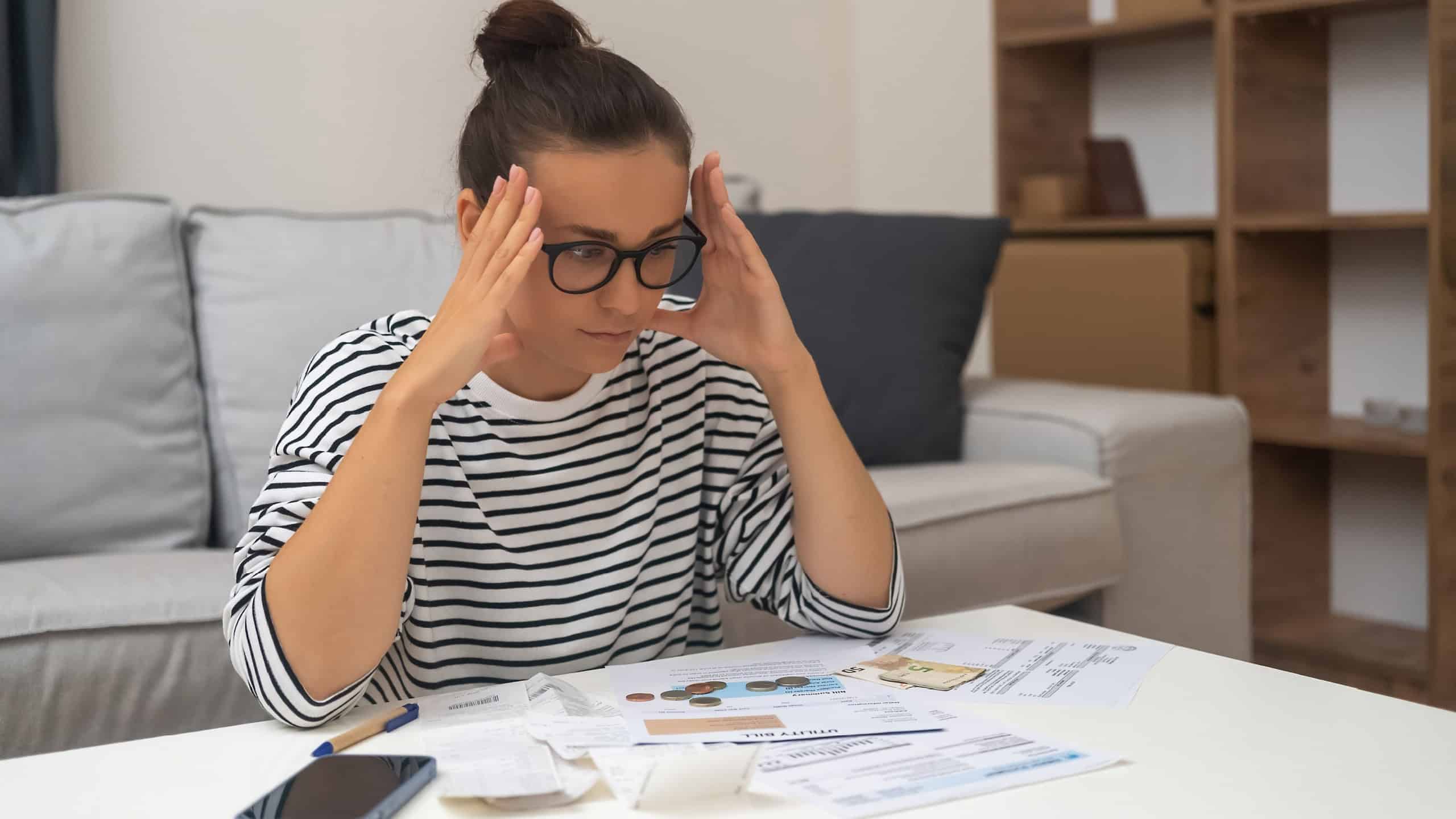 Budget Distress: Stressed by debt, a woman manages household finances, calculates expenses, and seeks solace in online payments while feeling unhappy.
