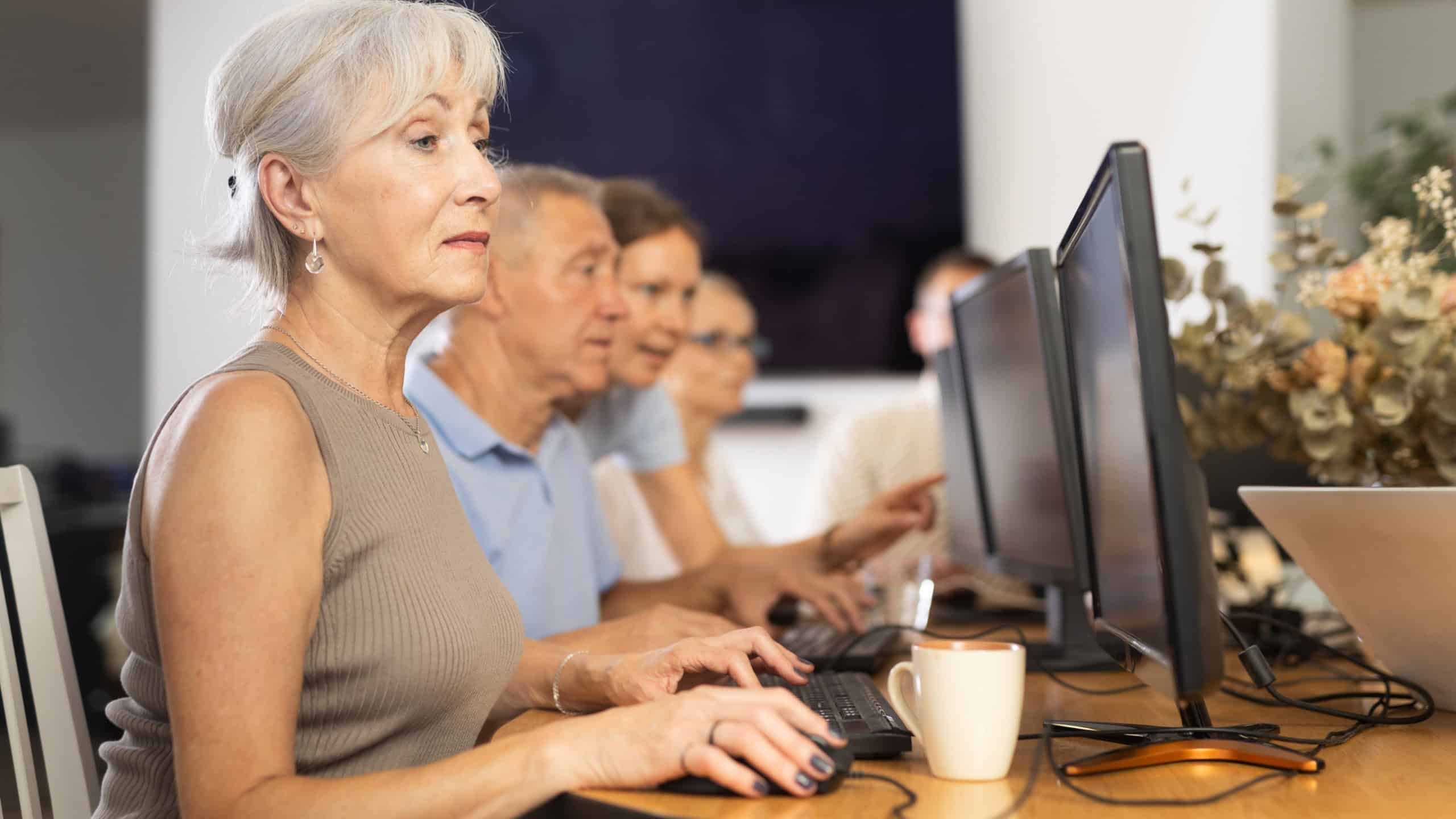 Gray-haired elderly lady engrossed in exploring digital realm at internet cafe, using computer, demonstrating curiosity of modern seniors towards technology
